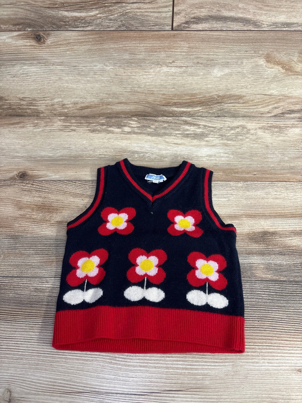 Navy blue toddler sweater vest with red trim and red, white, and yellow floral patterns on wood floor