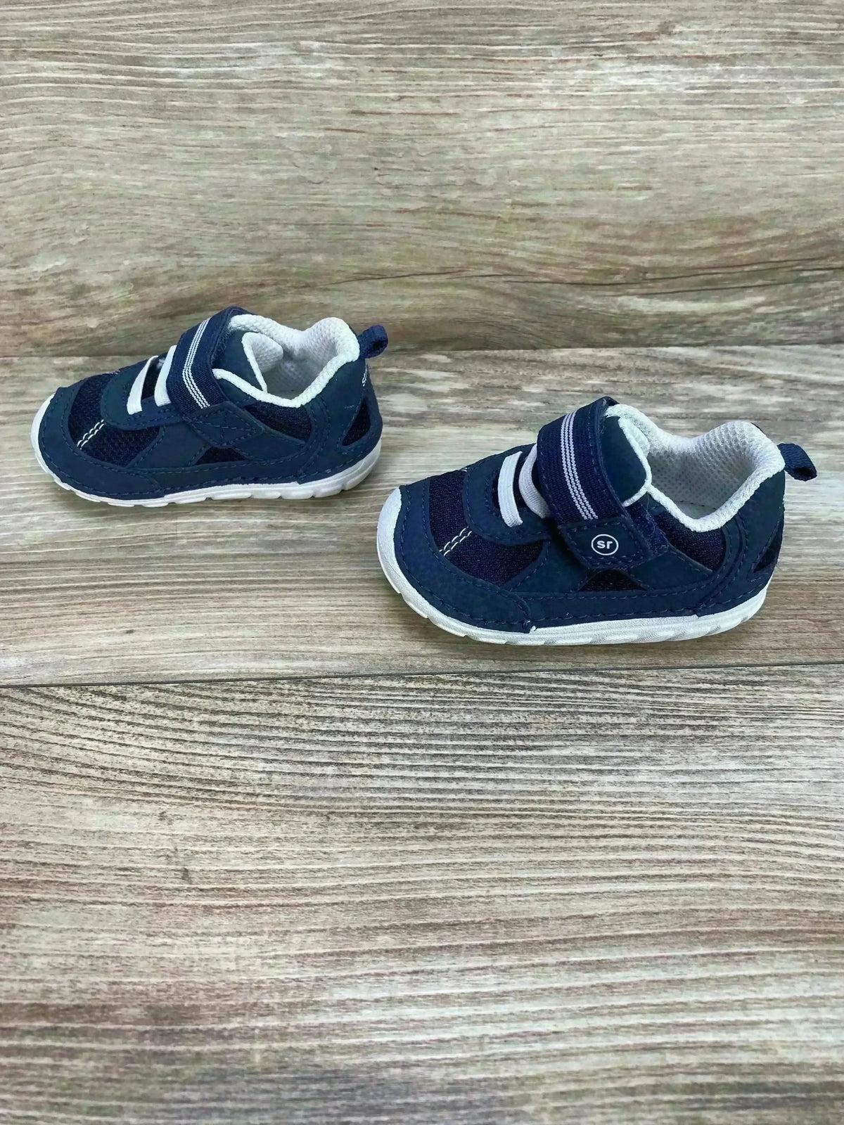 Side view of Stride Rite Jamie boys' navy and white toddler sneakers showing velcro strap and white sole on wood background