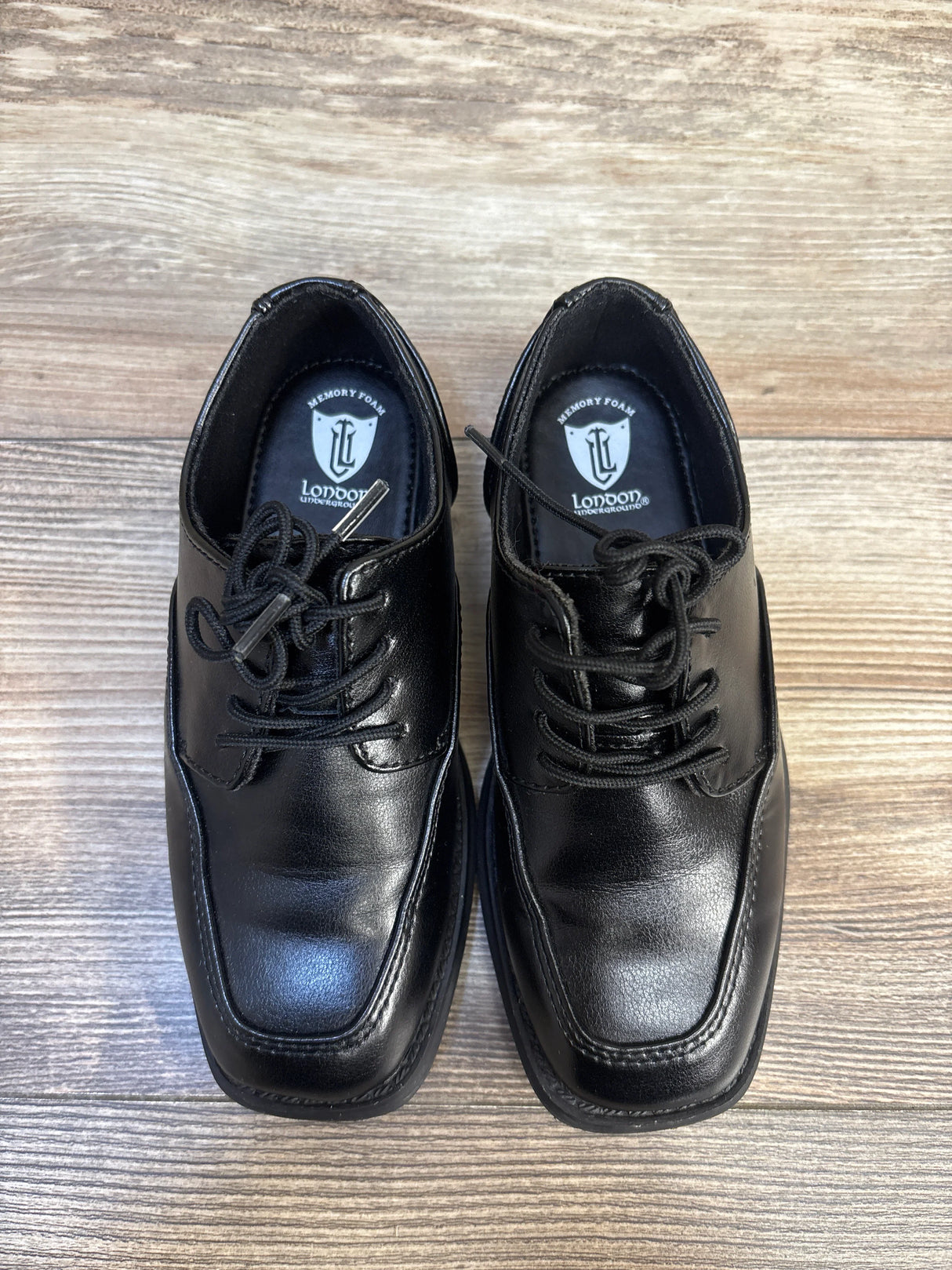 Black leather kids dress shoes with laces and memory foam insoles on wood floor
