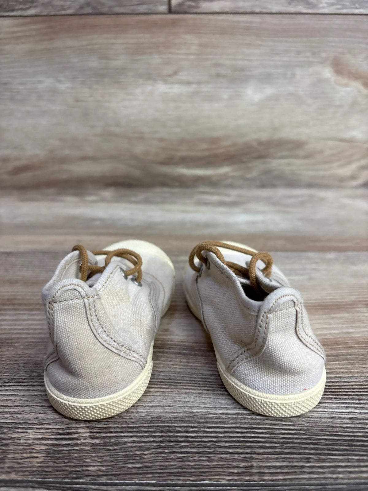 Pair of beige toddler canvas shoes with brown laces on wooden surface