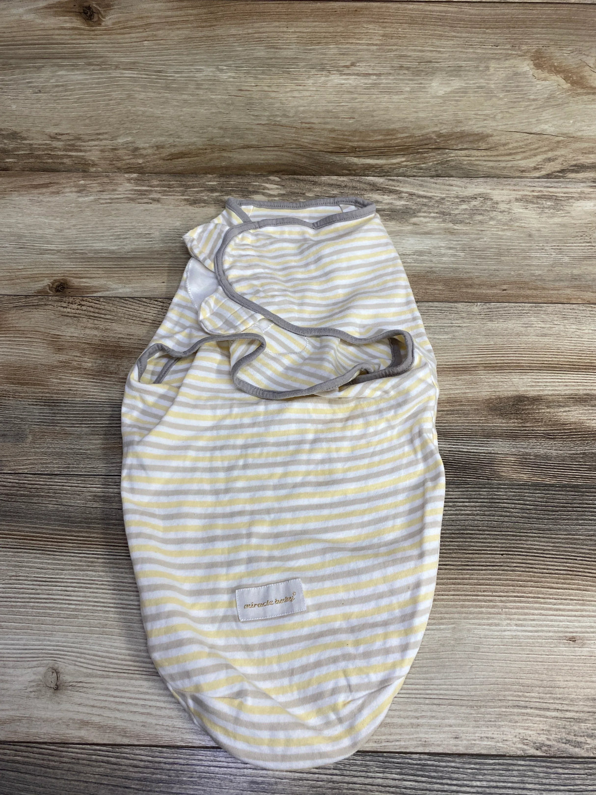 Striped yellow and white baby swaddle with grey trim on wooden surface