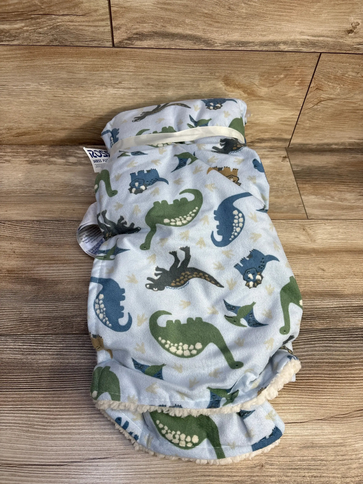 Folded blue baby blanket with green and blue dinosaur prints on wooden surface
