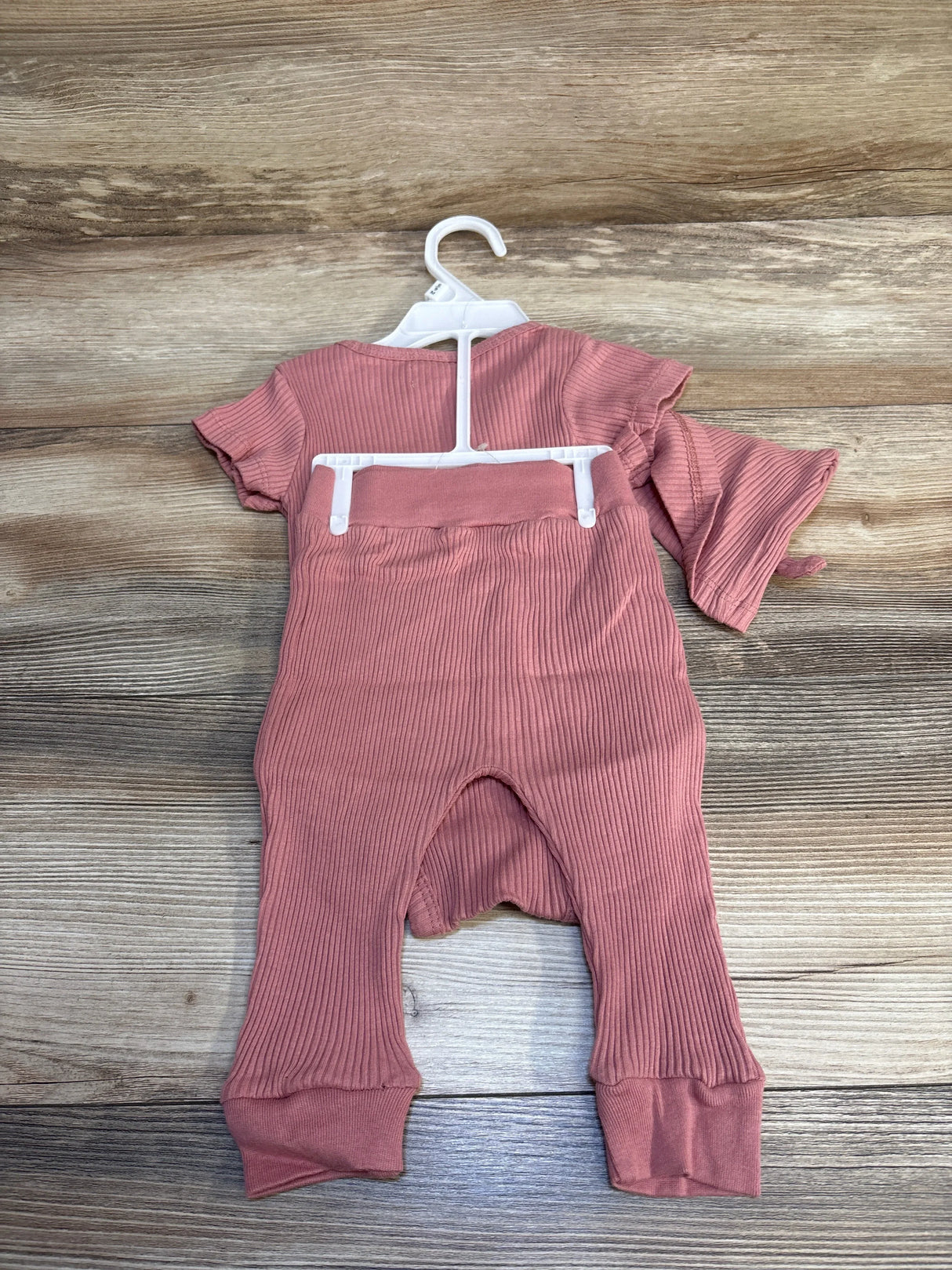 Ribbed pink baby romper with short sleeves on hanger, displayed on wood background