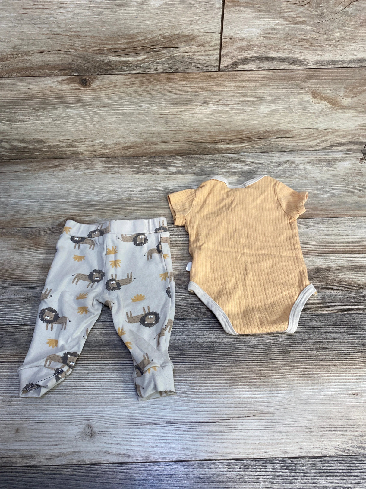Baby outfit set with lion print pants and ribbed beige onesie on wooden background