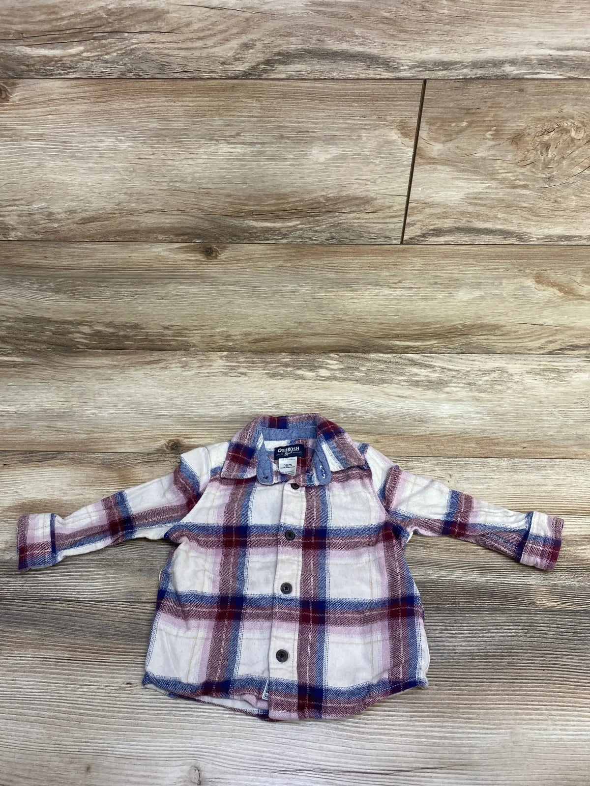 Flat lay of OshKosh 18M long-sleeve plaid flannel button-up shirt showing spread collar and buttons on light wood floor