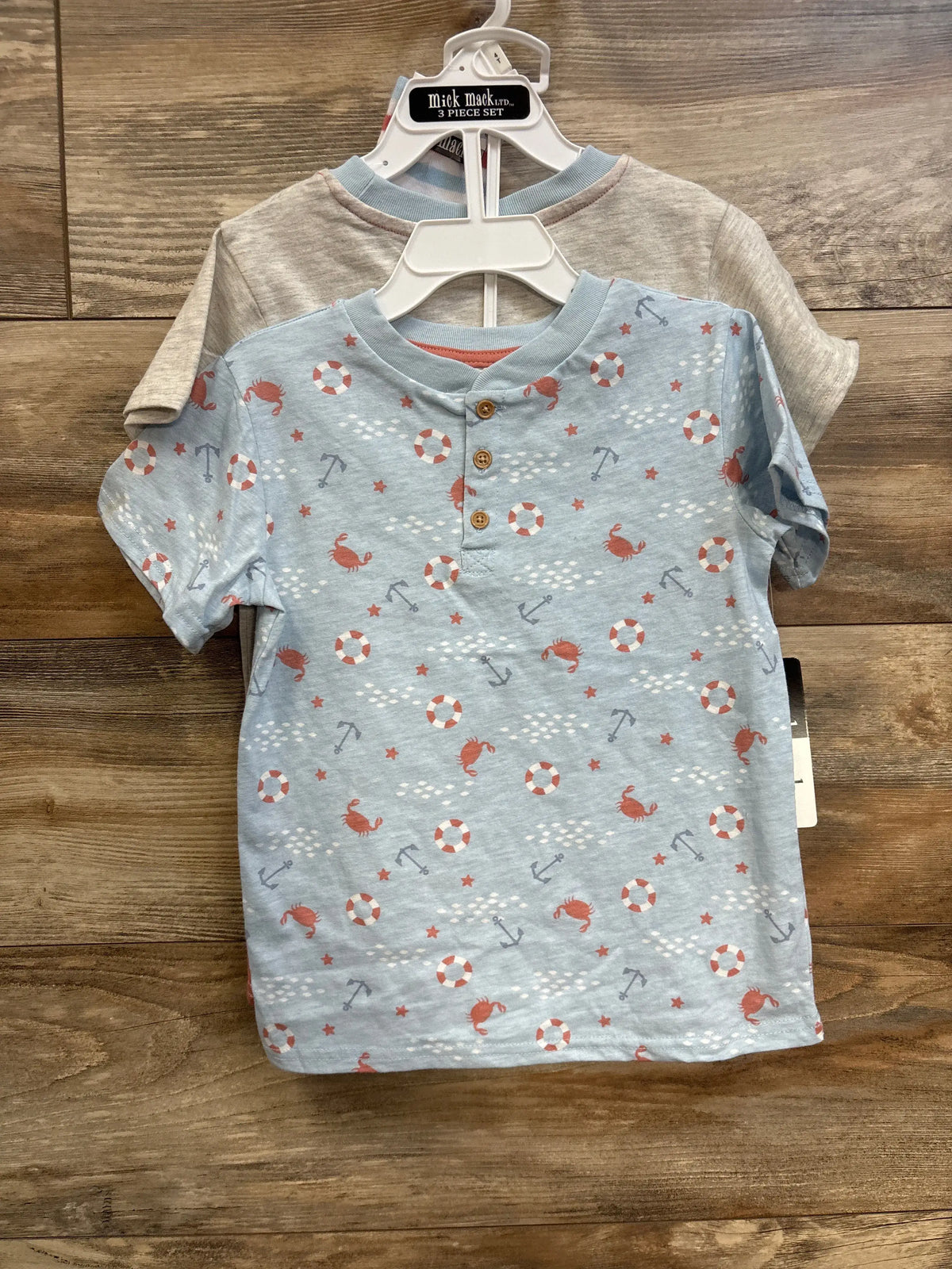 Front view of blue Mick Mack short-sleeve shirt from 4-piece set showing crab, anchor, and lifesaver print on wood background