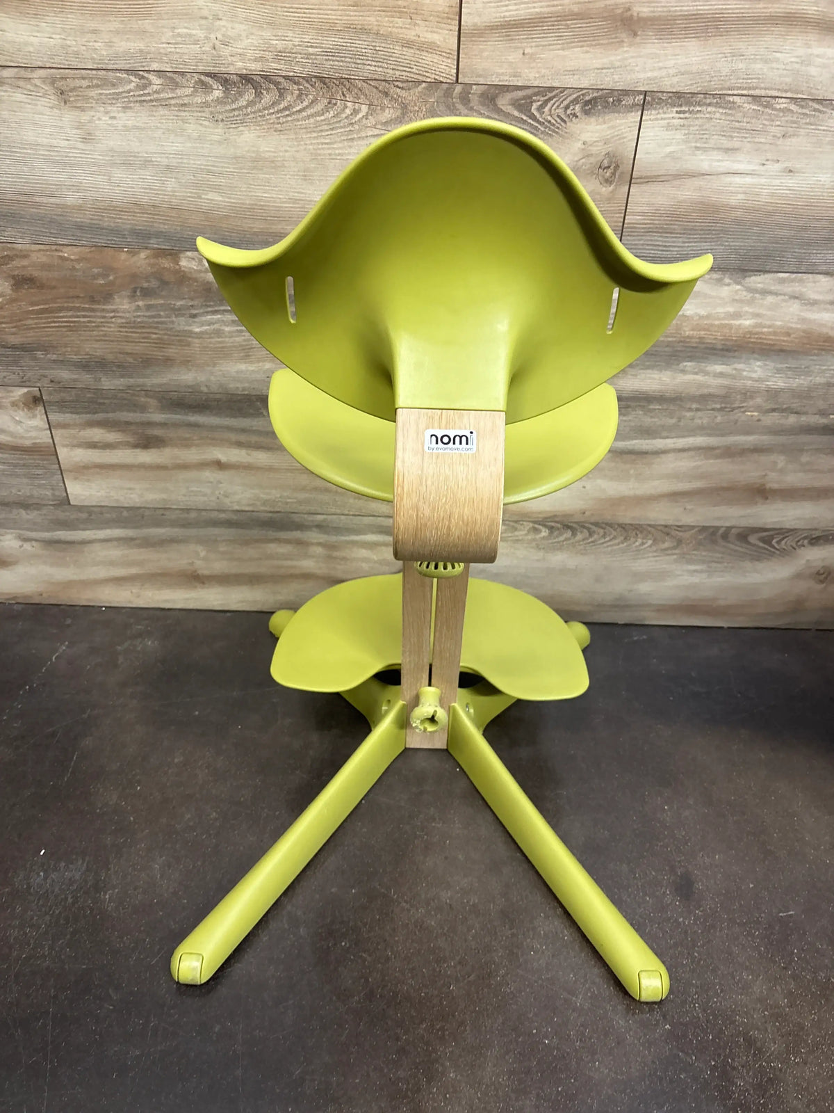 Back view of Stokke Nomi adjustable high chair showing green seat and wood center support on wood wall and dark floor