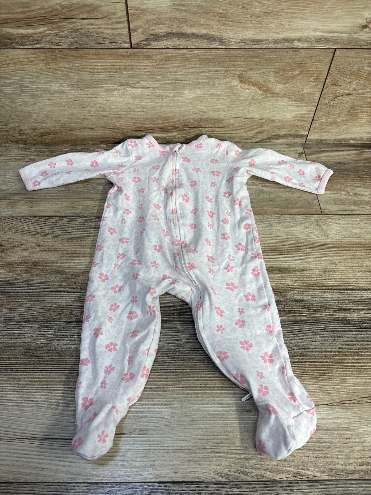 Top-down view of a white floral sleeper showcasing a pink flower pattern and front zipper on a wood-look floor