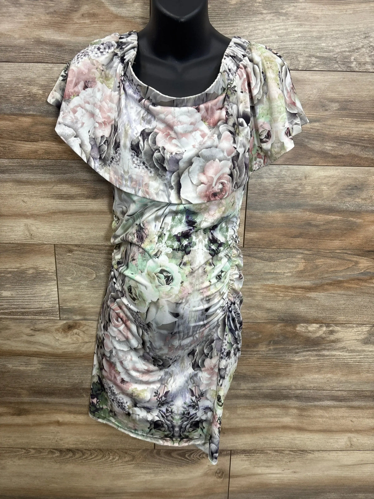 Floral maternity dress with pastel rose pattern and ruched sides on mannequin, wood background