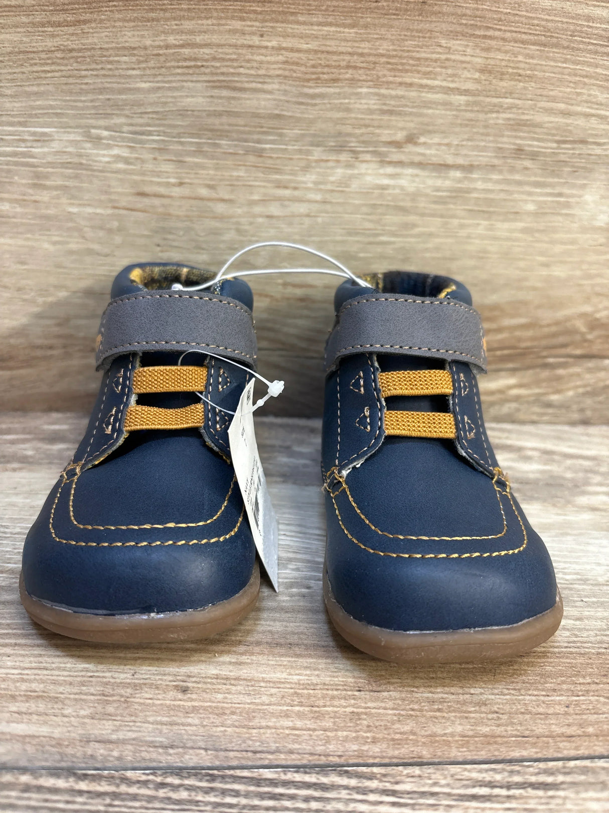 Navy blue toddler shoes with yellow laces and gray Velcro straps on a wood background