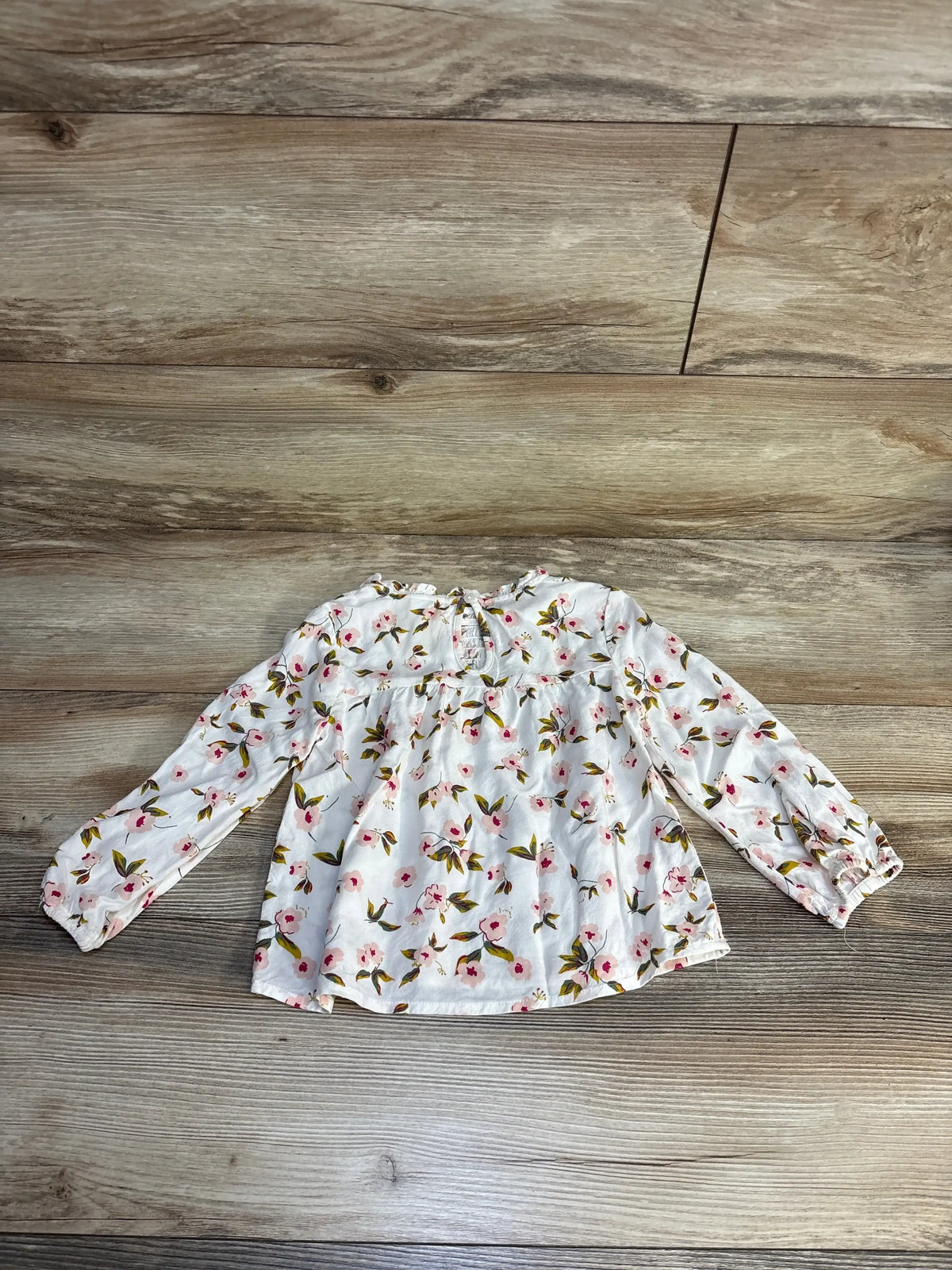 White floral baby girl long sleeve top with pink flowers and green leaves on wood floor