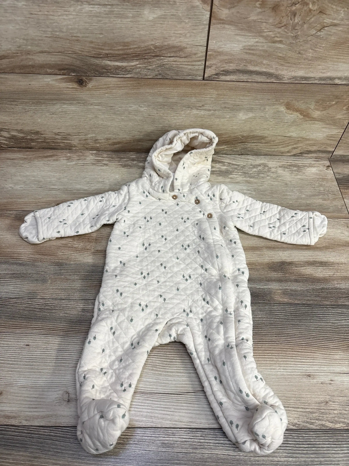 White quilted baby onesie with hood and button details, patterned with small gray dots, laid flat on wood floor