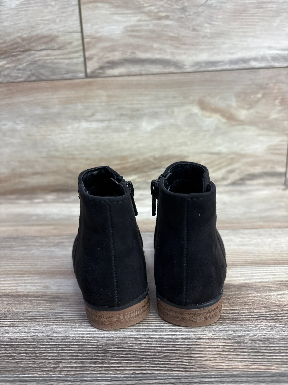 Pair of black suede toddler ankle boots with brown soles on wood floor