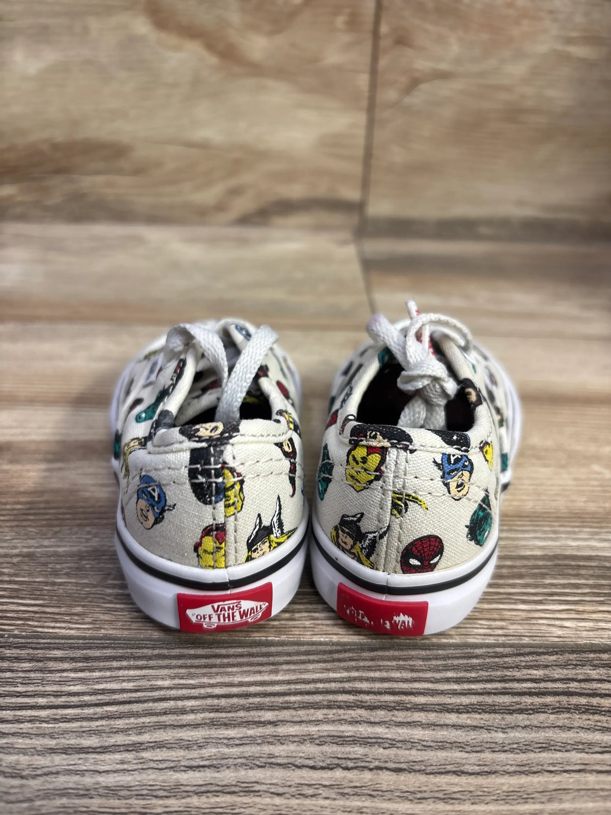 Rear view of cream Vans x Marvel Authentic sneakers showcasing Marvel character print and red Vans heel labels on wood