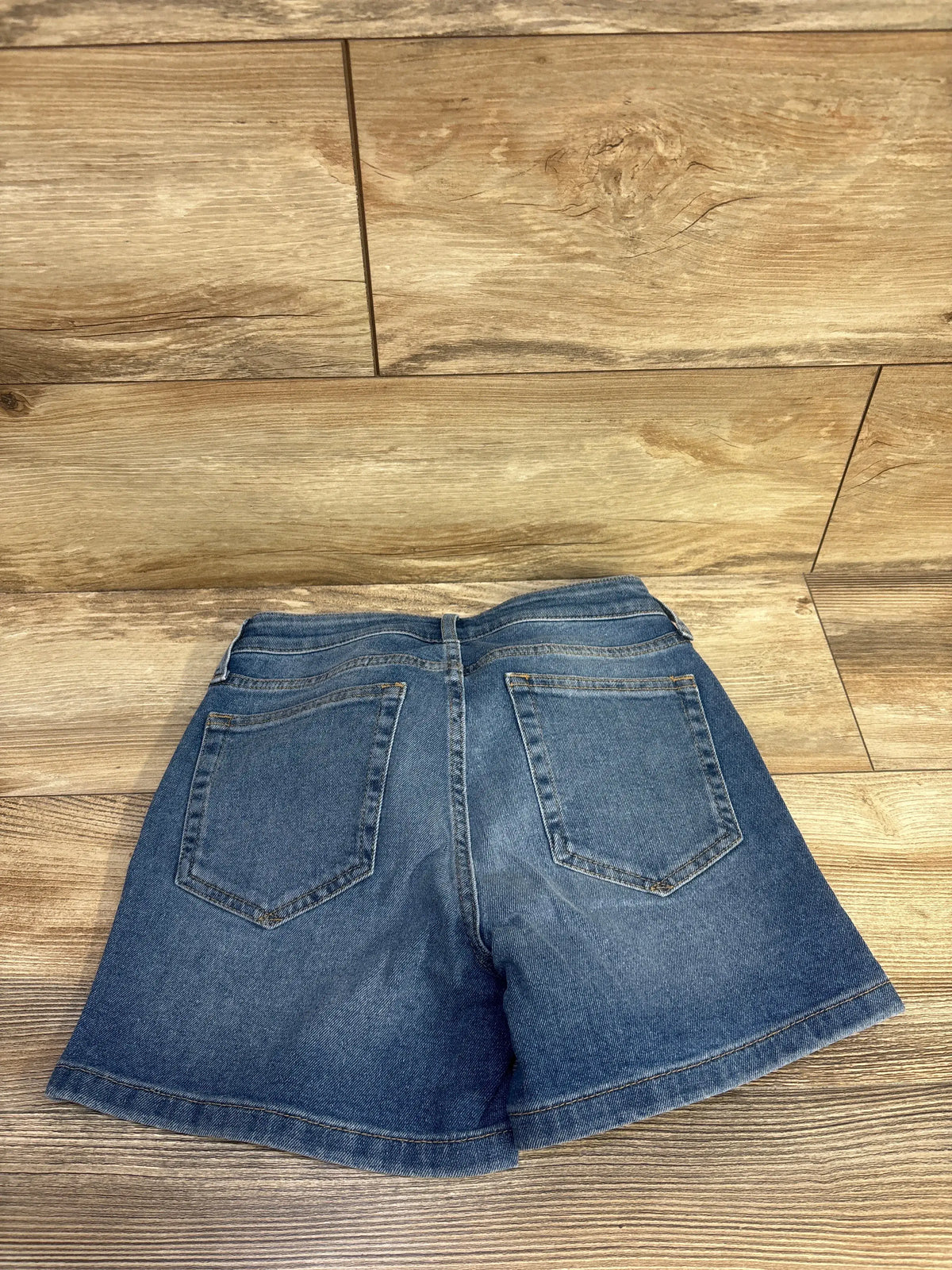 Back view of Gap maternity 4 inch inset panel denim shorts showcasing two back pockets on a wood floor