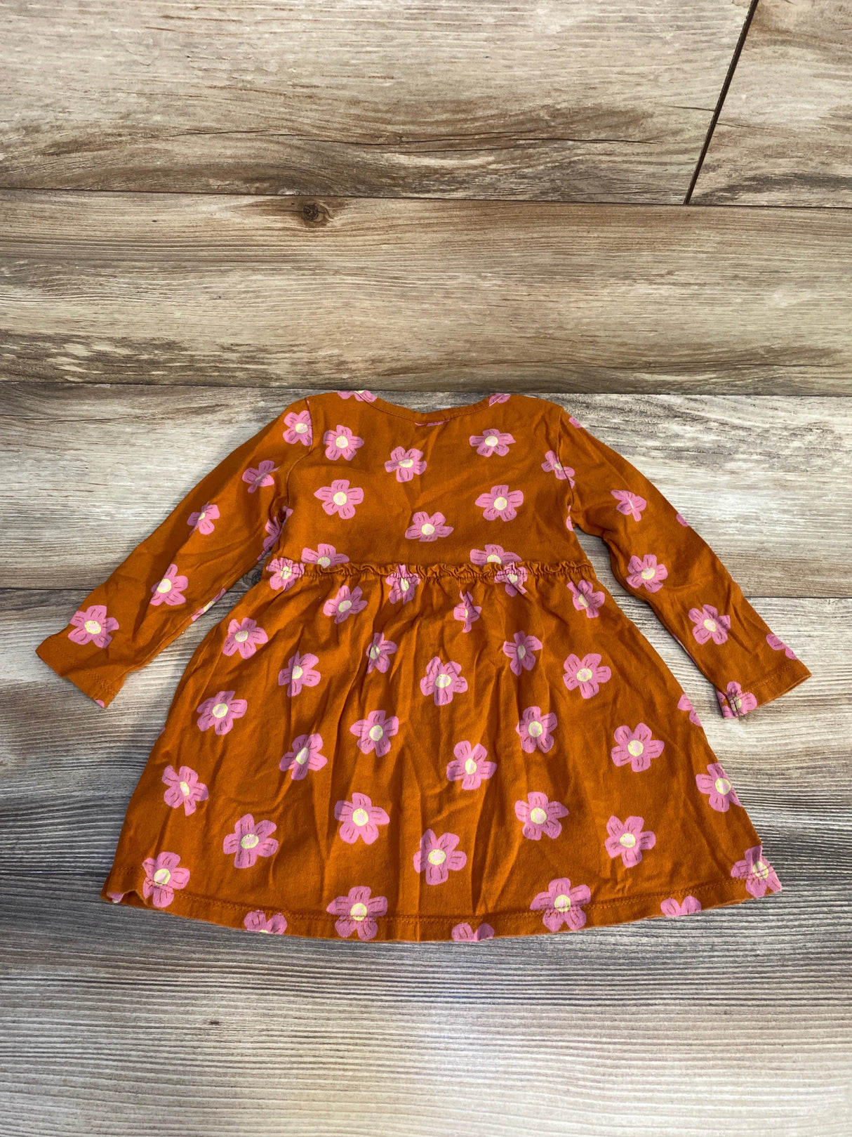 Rust orange long sleeve toddler dress with pink flower print on wood background