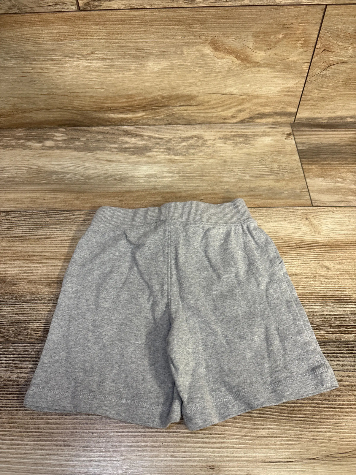 Front view of Carter’s grey drawstring shorts in size 24 months showcasing the elastic waistband and relaxed fit on a wood floor