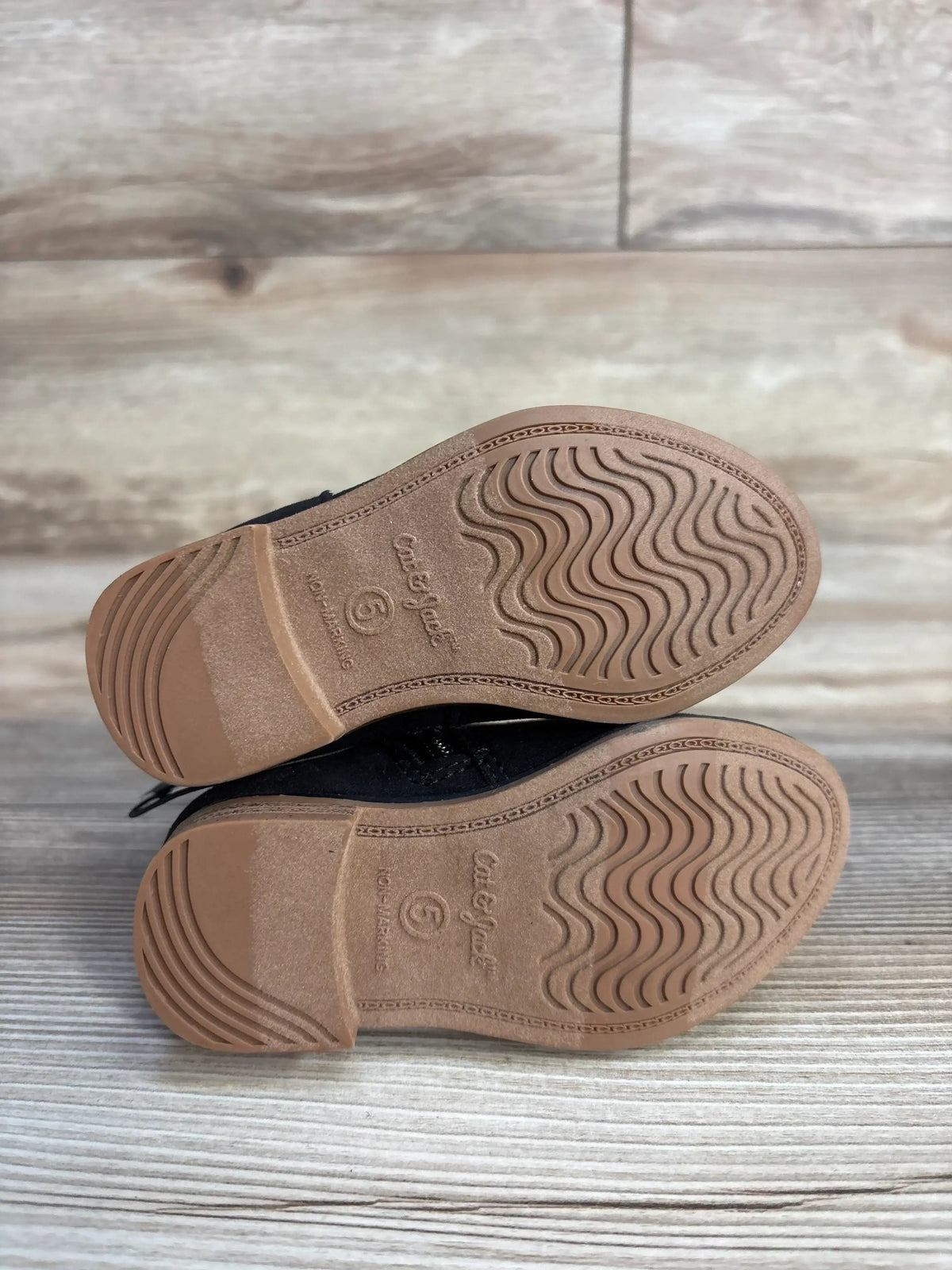 Bottom view of Cat & Jack Penelope zipper booties in black showing brown rubber soles with wave tread and size 5 marking on wood background