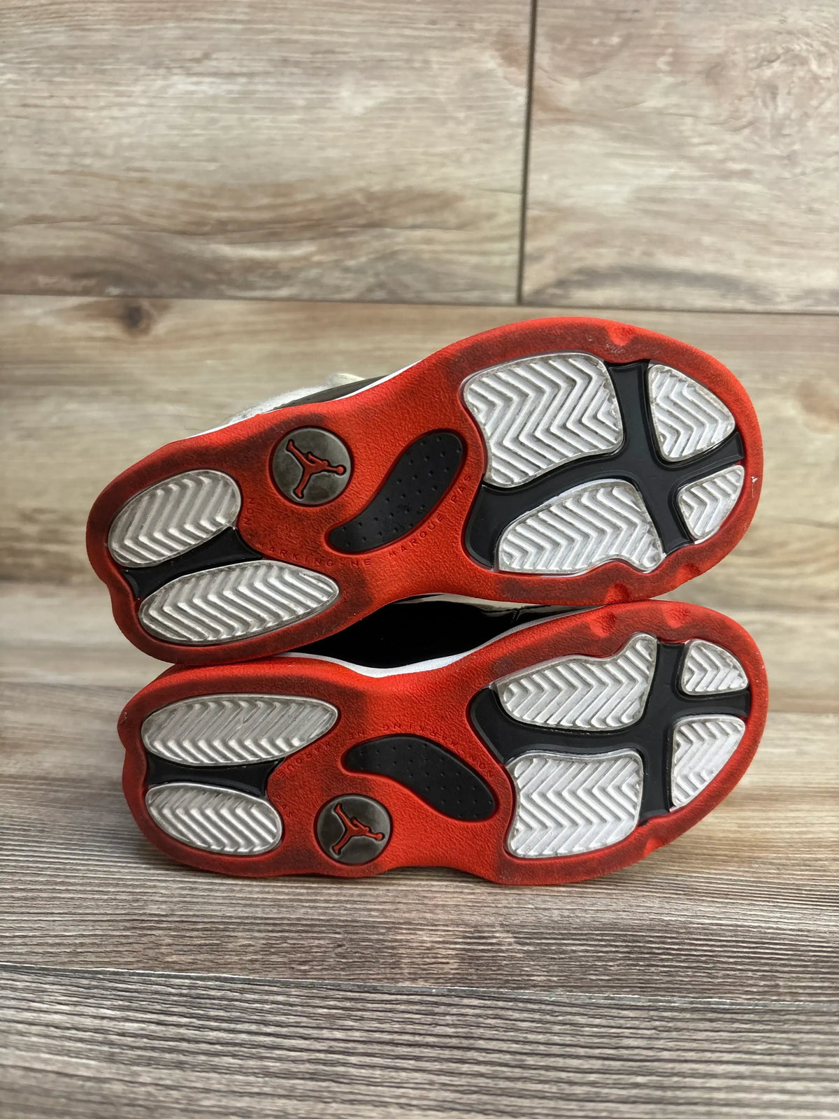 Soles view of Air Jordan 6 Rings TD toddler sneakers showing red and black outsoles with silver Jumpman logos on wood floor