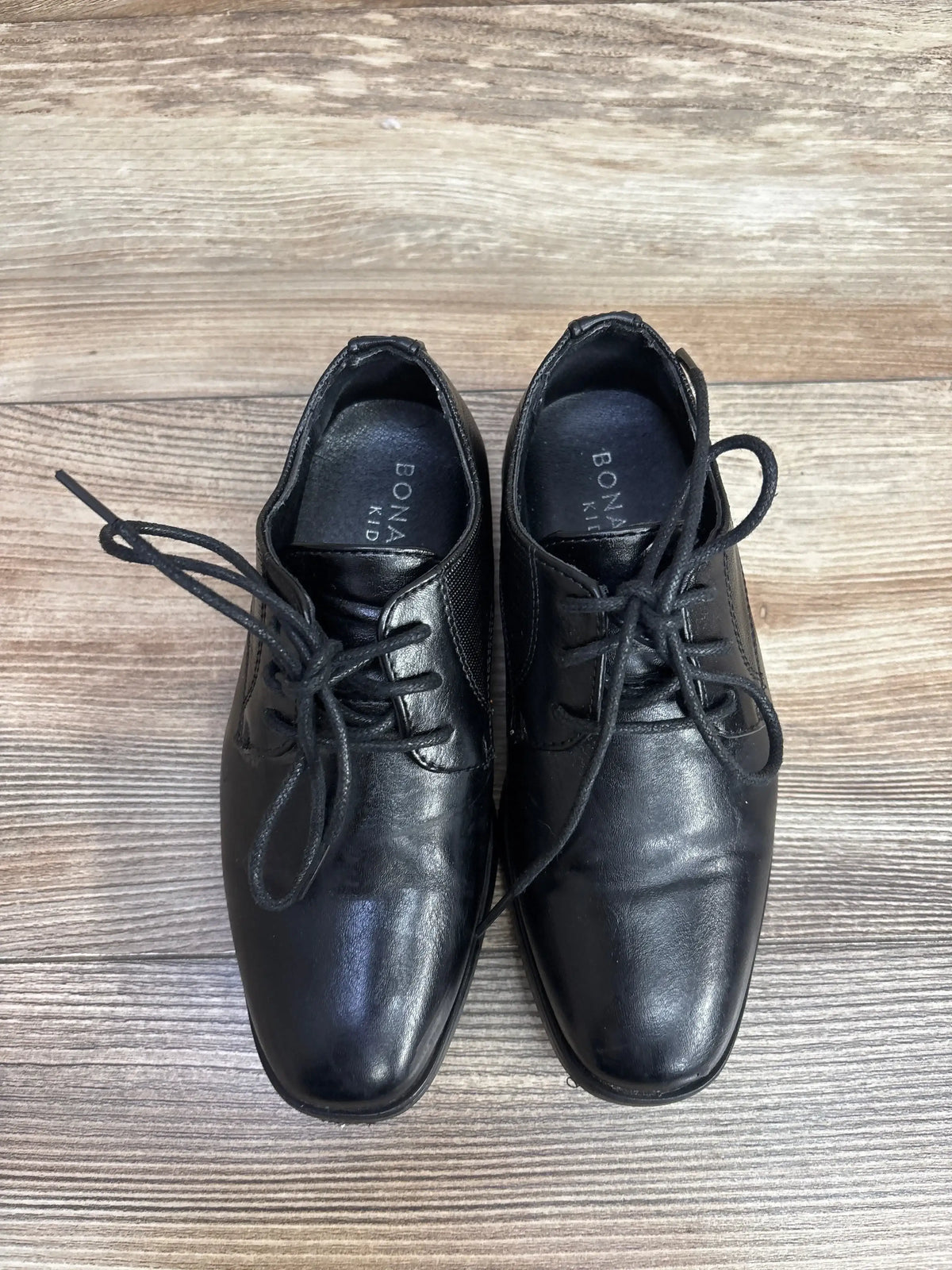 Top view of Bonafini Kids K-154 leather dress shoes showcasing square toes, lace-up fronts, and elastic side panels on wood floor