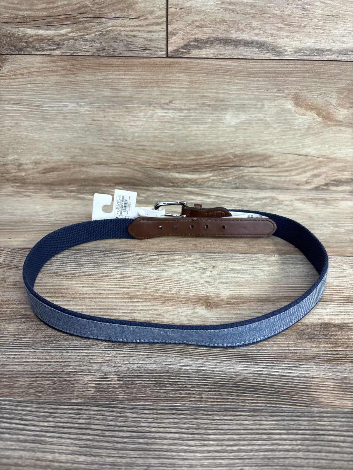 Blue fabric belt with brown leather details and silver buckle on wooden background