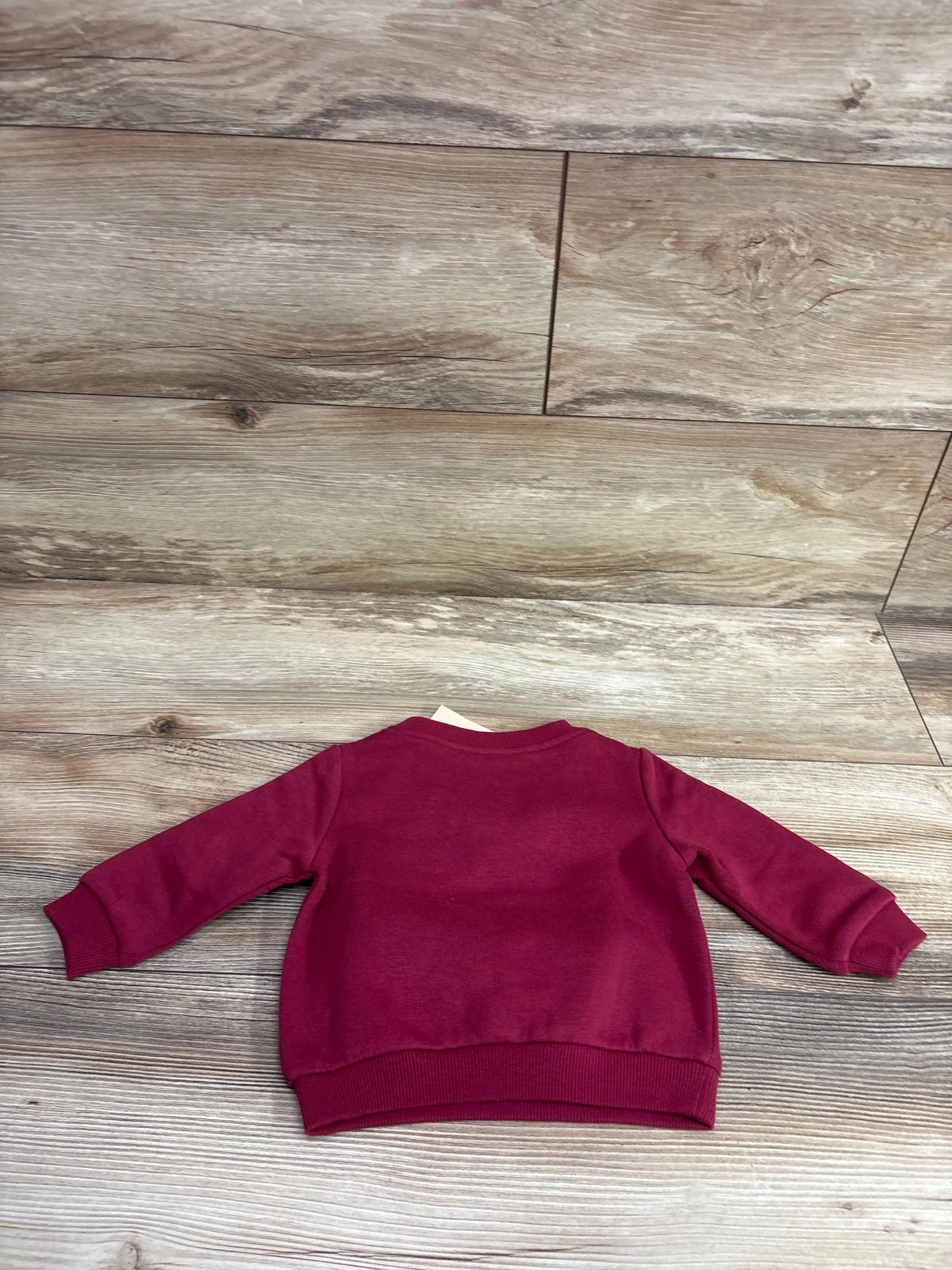 Maroon First Impressions pullover sweatshirt for babies size 3-6m on a wood background