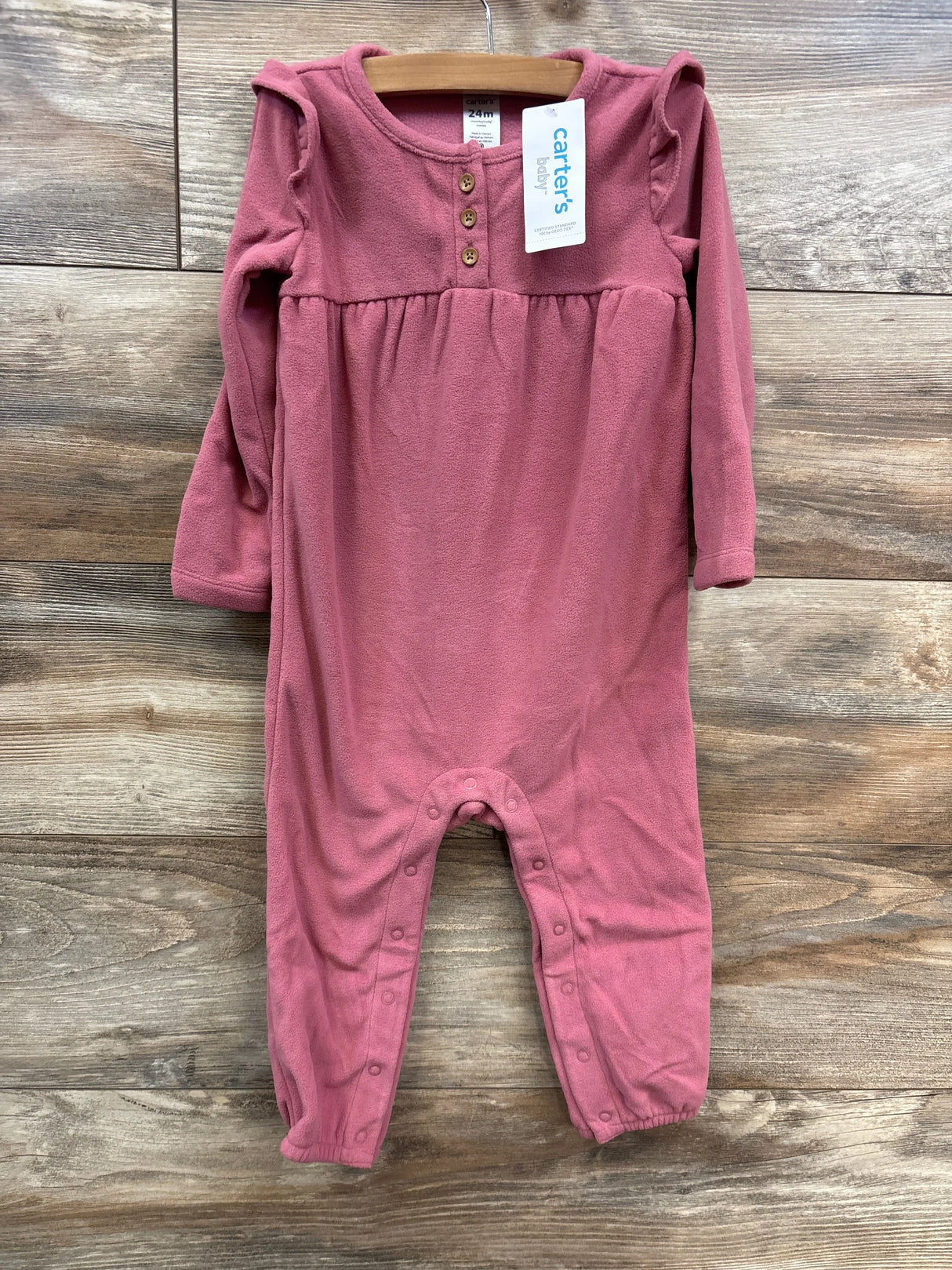 Carter's baby fleece pink jumpsuit with long sleeves, button details, and snap closures on rustic wooden background