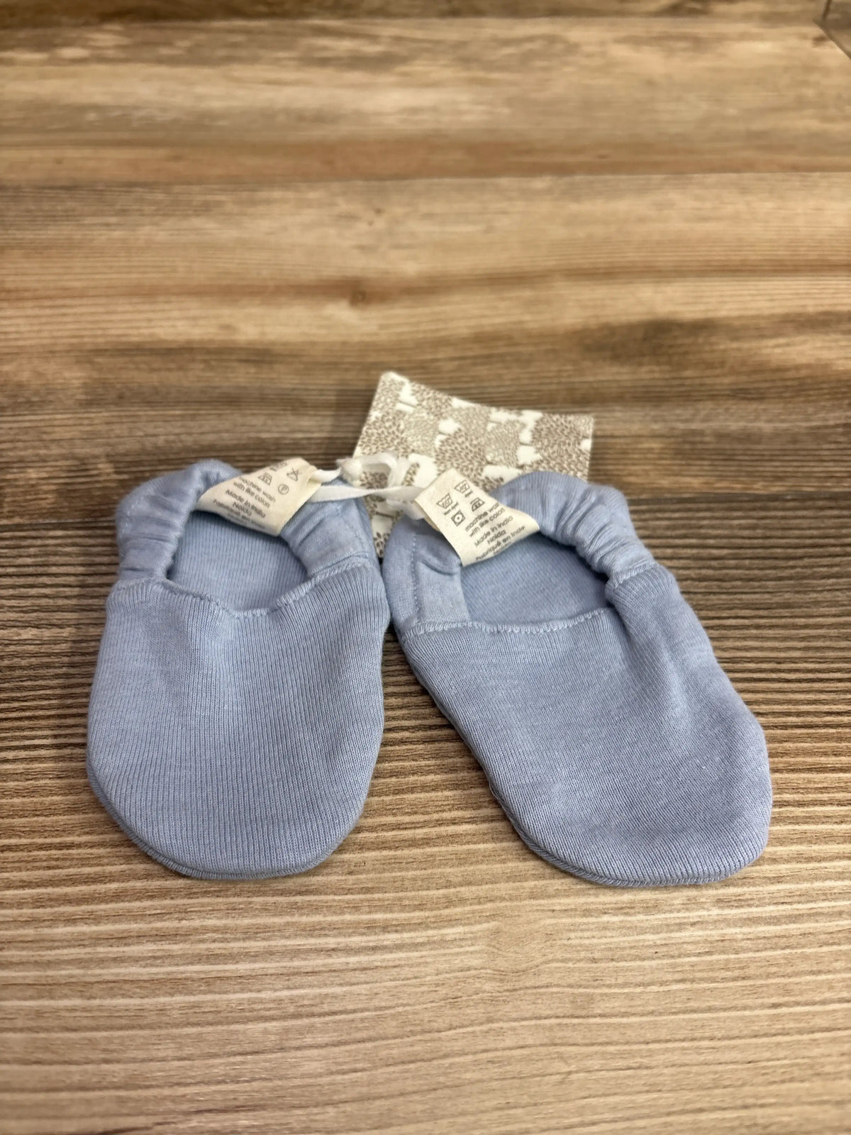 Top view of blue Kate Quinn booties for ages 6 to 12 months, showing elastic ankle openings on a wood-grain surface