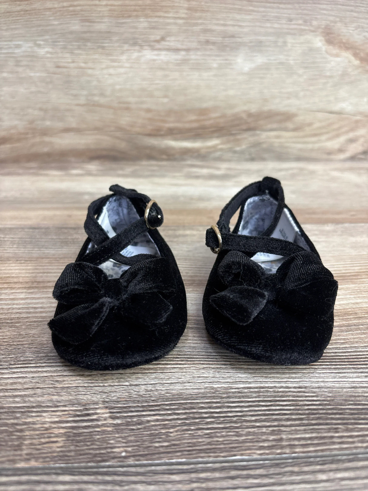 Black velvet baby shoes with bows and ankle straps on wooden background