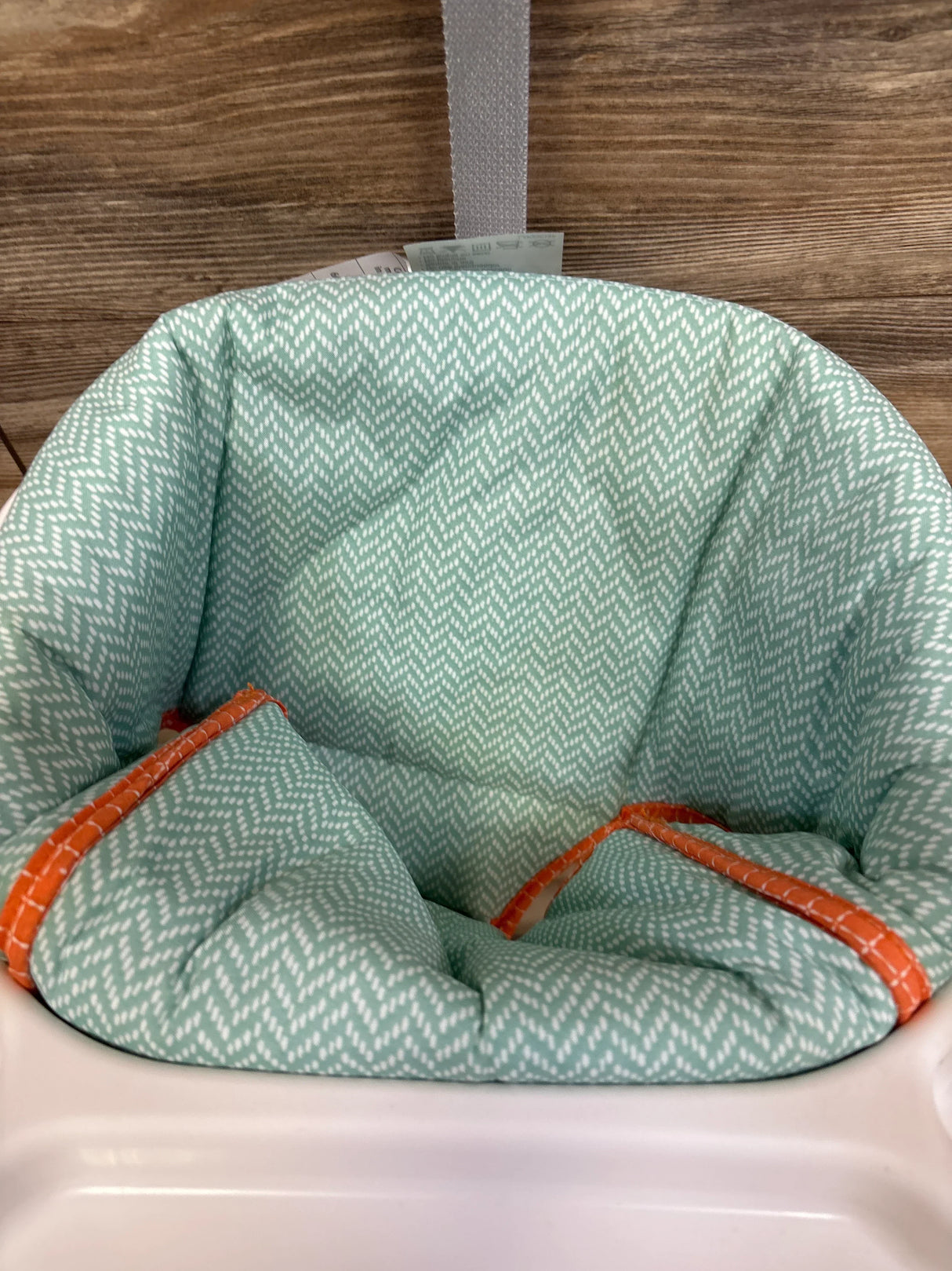 Close-up of mint green high chair cushion with white chevron pattern and orange trim against wood plank wall