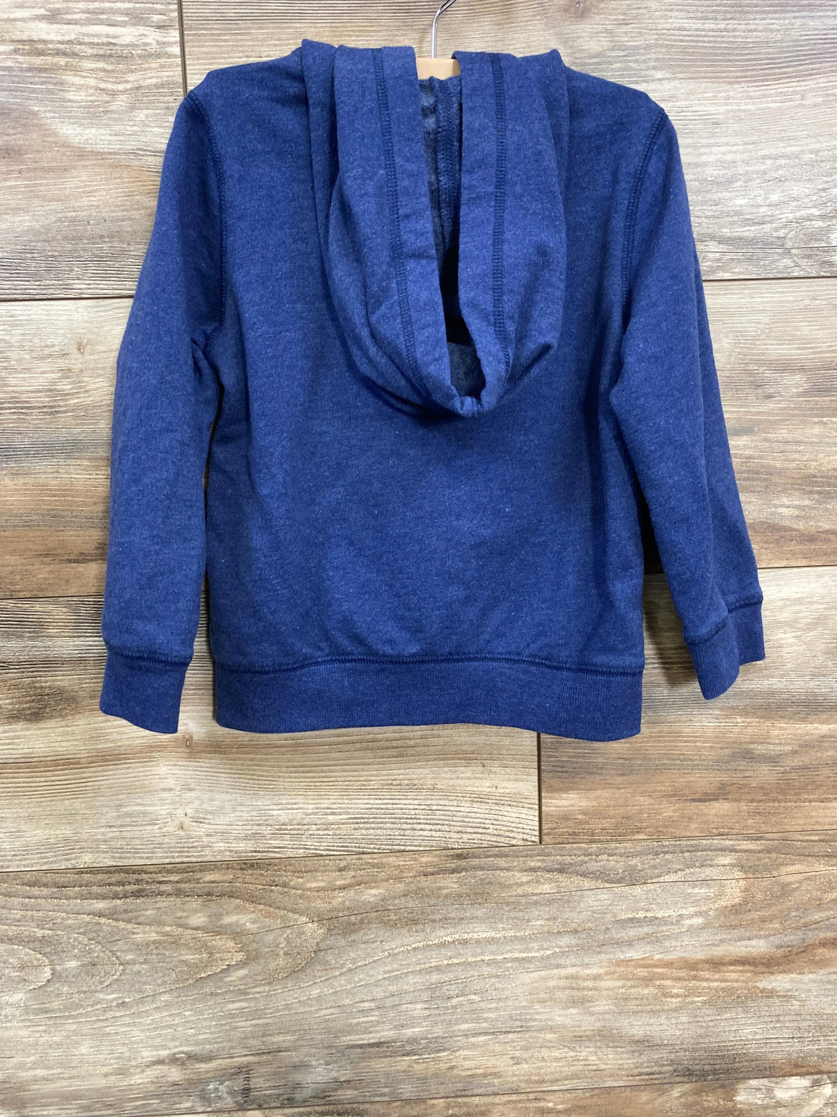Back view of a navy blue children's hoodie on wooden hanger against wood panel background