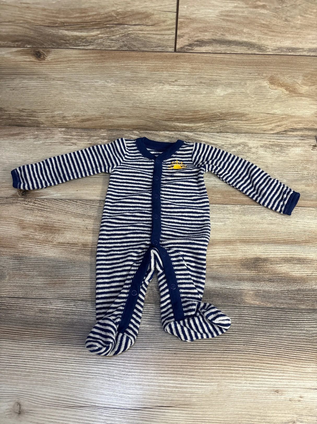 Flat lay of navy and white striped terry cloth newborn footed sleeper with front snaps and sun embroidery on wood floor