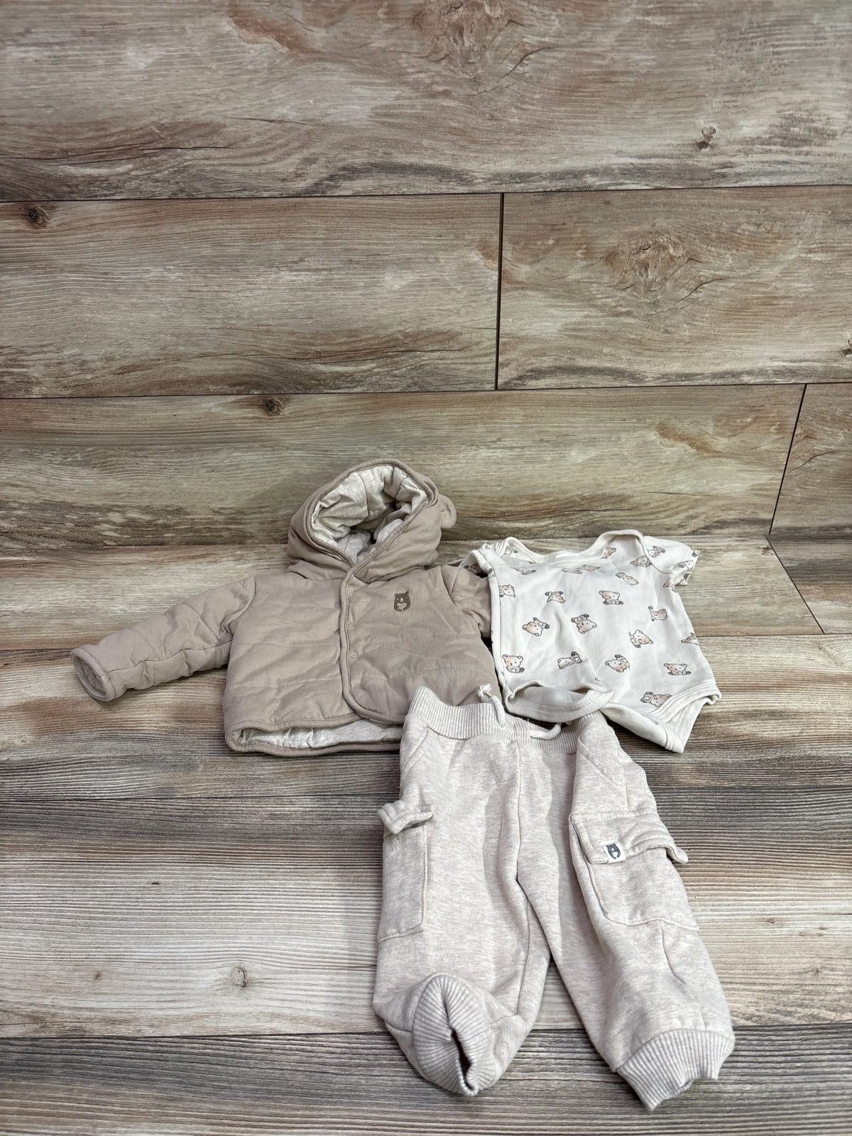 Top view of tan Rabbit and Bear three-piece set with hooded jacket, bear-print bodysuit, and pocketed pants on wood