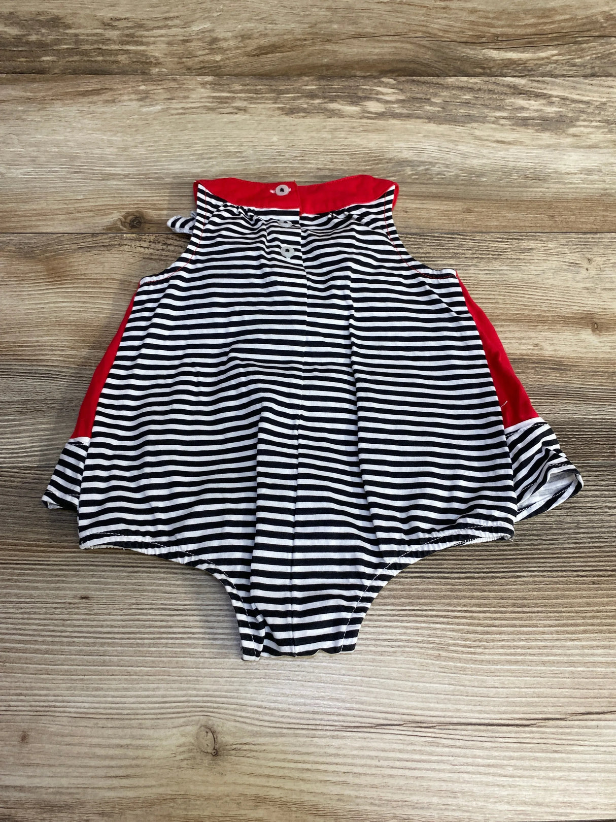 Flat-lay front view of watermelon skirted sunsuit, size 3-6M, showing black-and-white stripes and red trim on wood background
