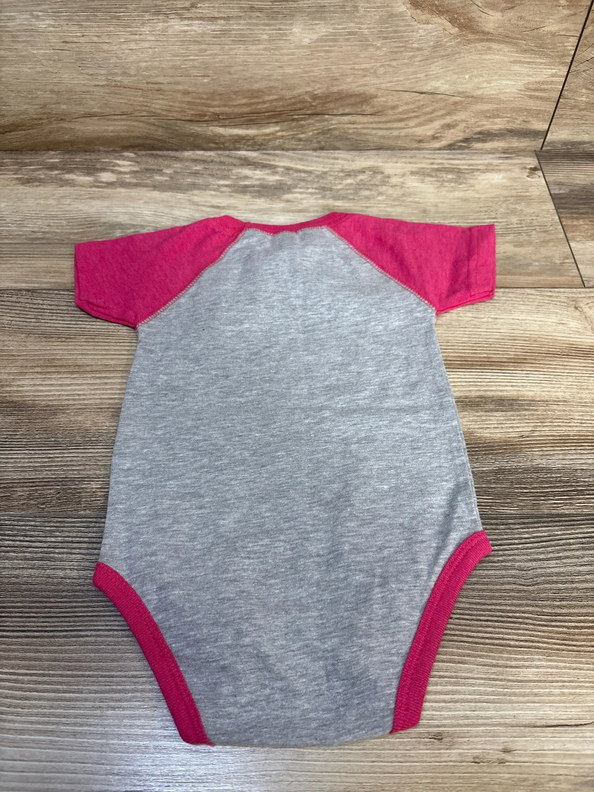 Top-down view of Rabbit Skins baby bodysuit, gray with pink raglan sleeves and pink trim, on wood background