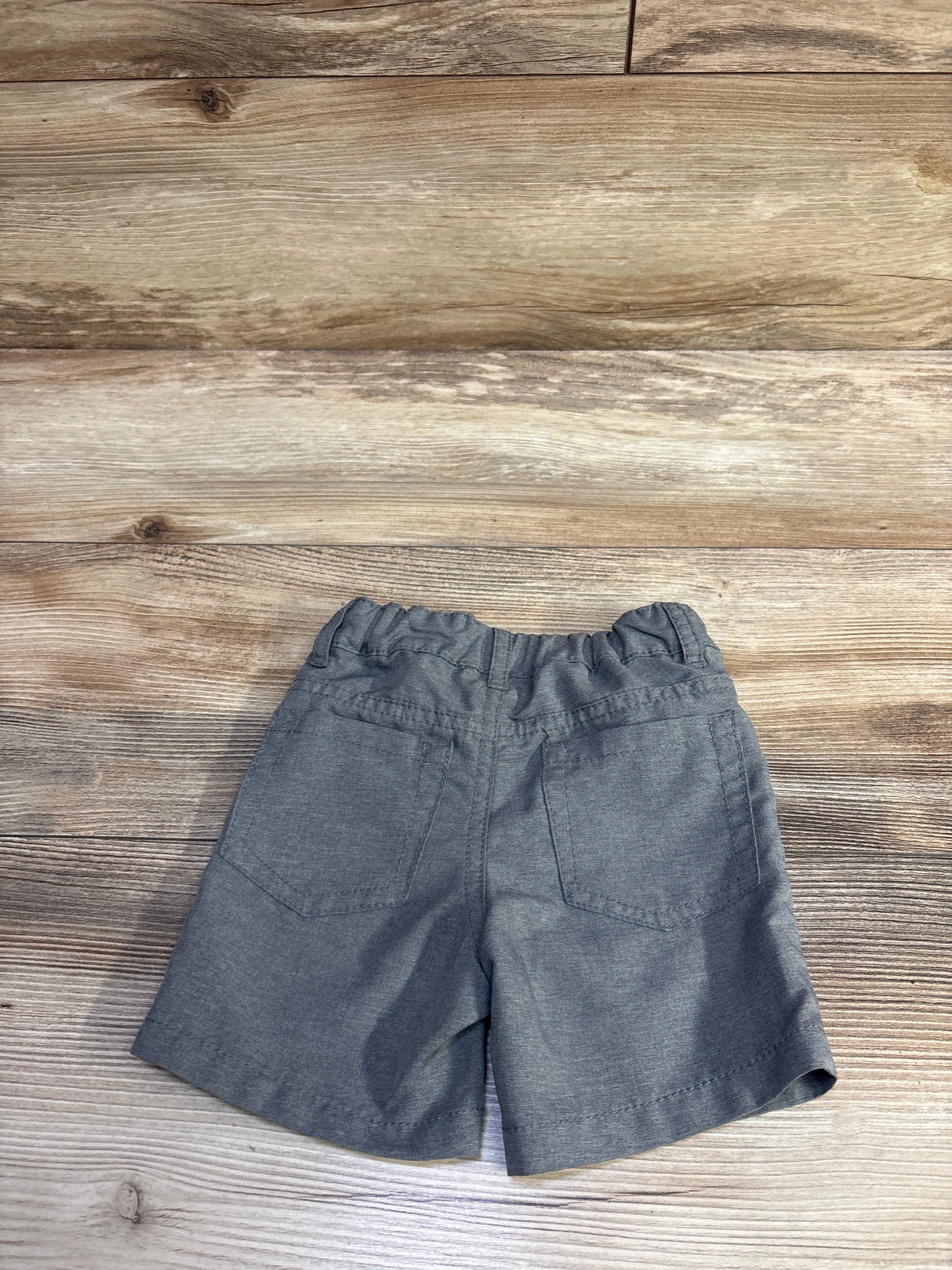 Back view of Cat & Jack toddler quick dry grey chino shorts showing elastic waistband and two patch back pockets on wood plank background