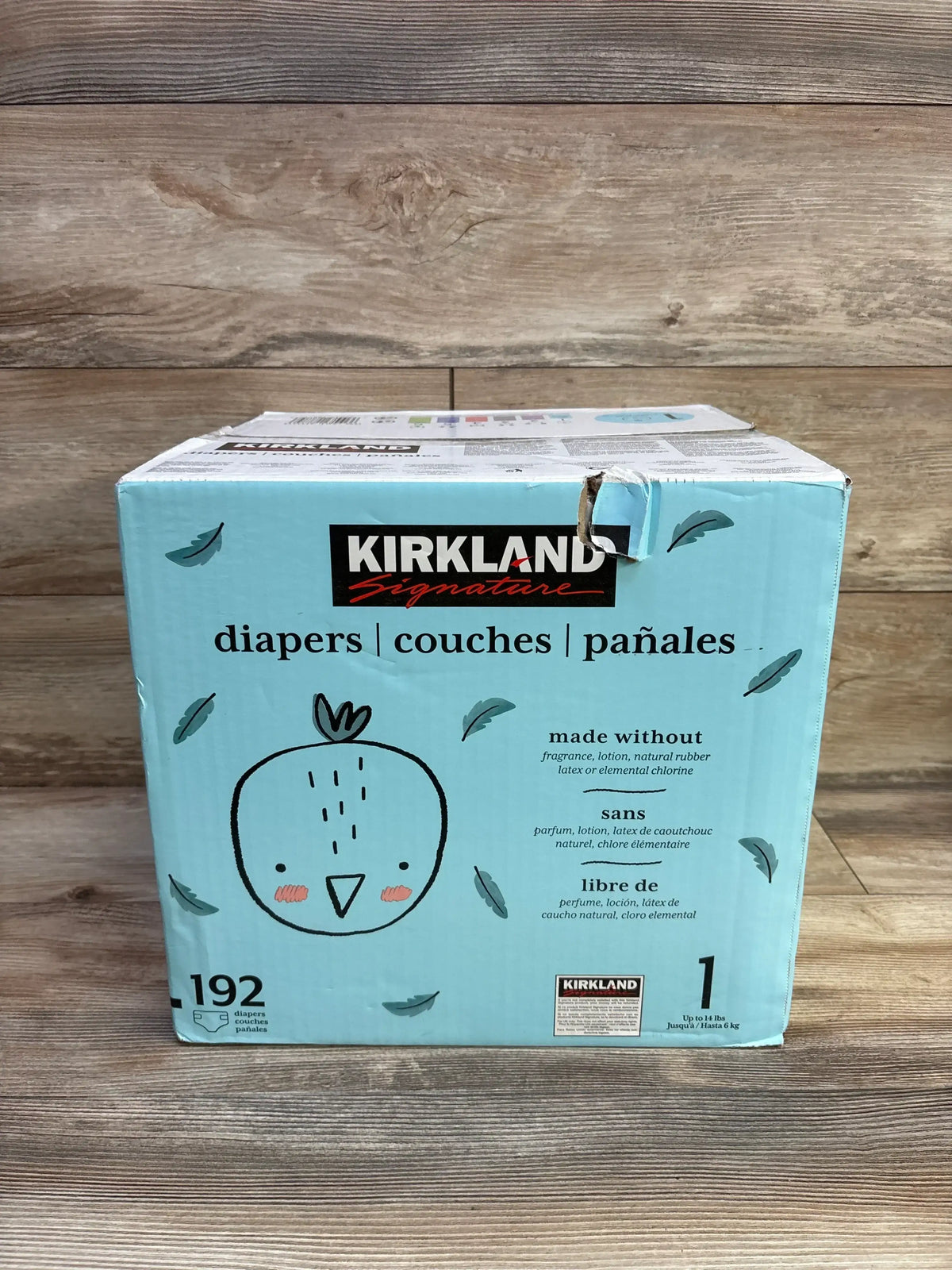 Front view of Kirkland Signature Size 1 diaper box showing 192-count packaging and 'made without' ingredient claims on a wood background