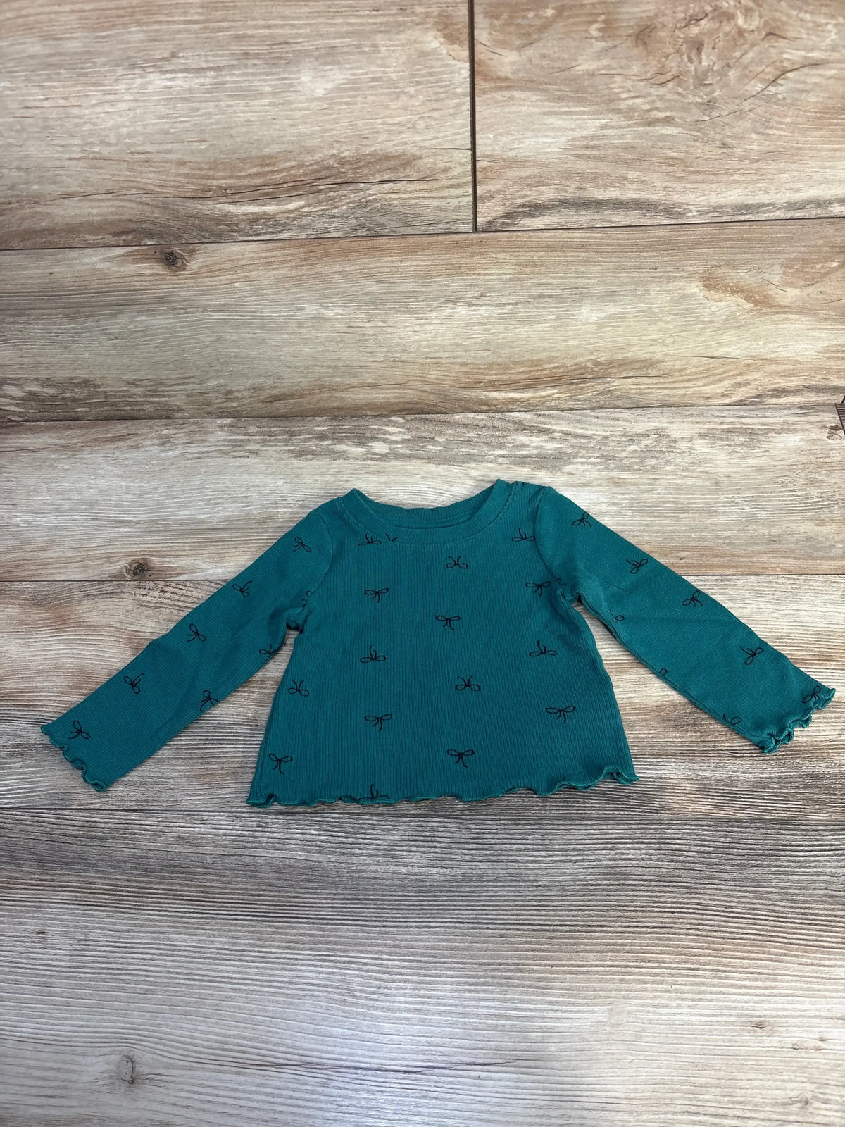 Teal long sleeve toddler shirt with small black bow prints on wood background
