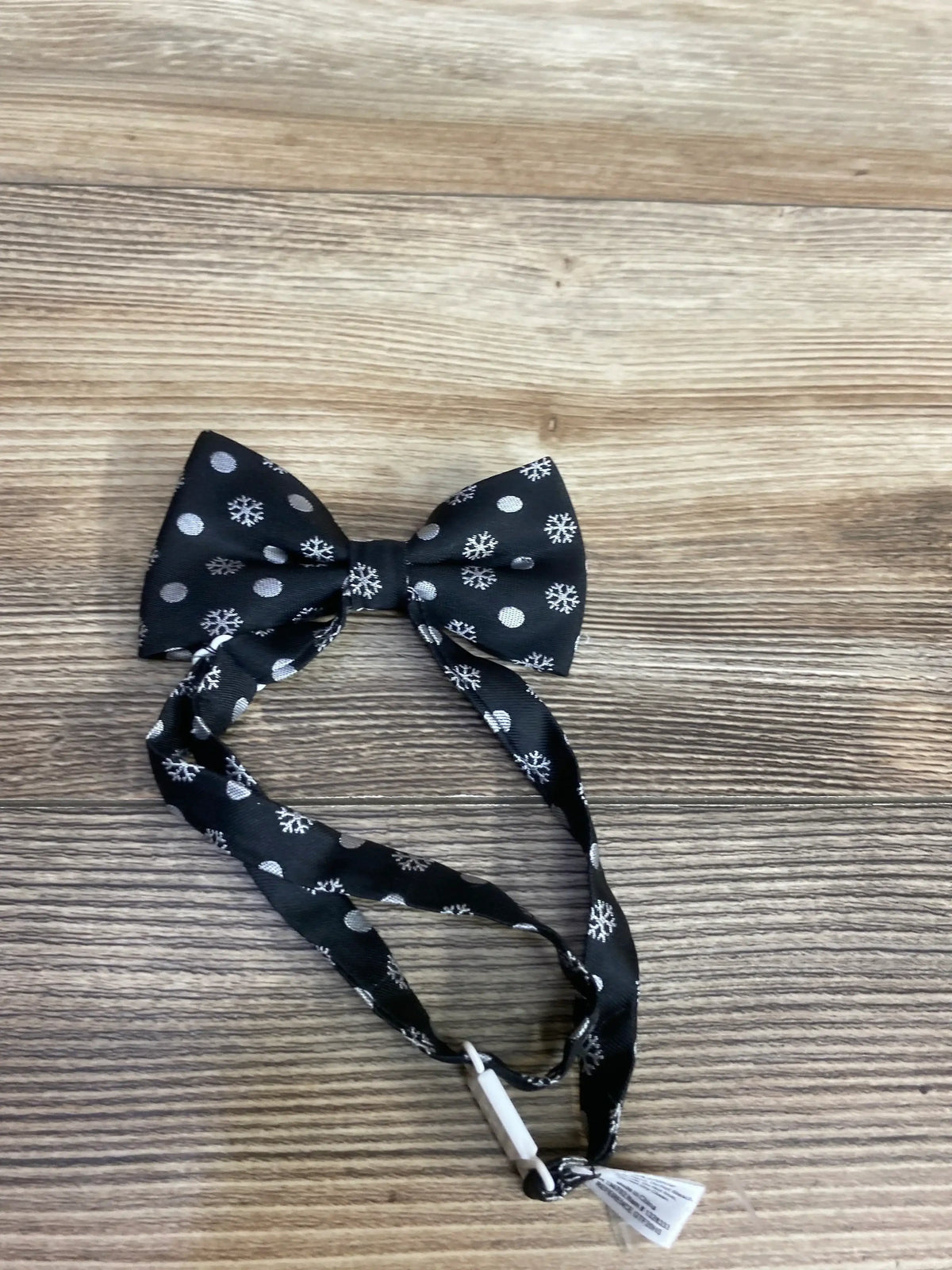 Black kids bow tie with white snowflake and dot pattern on wood surface