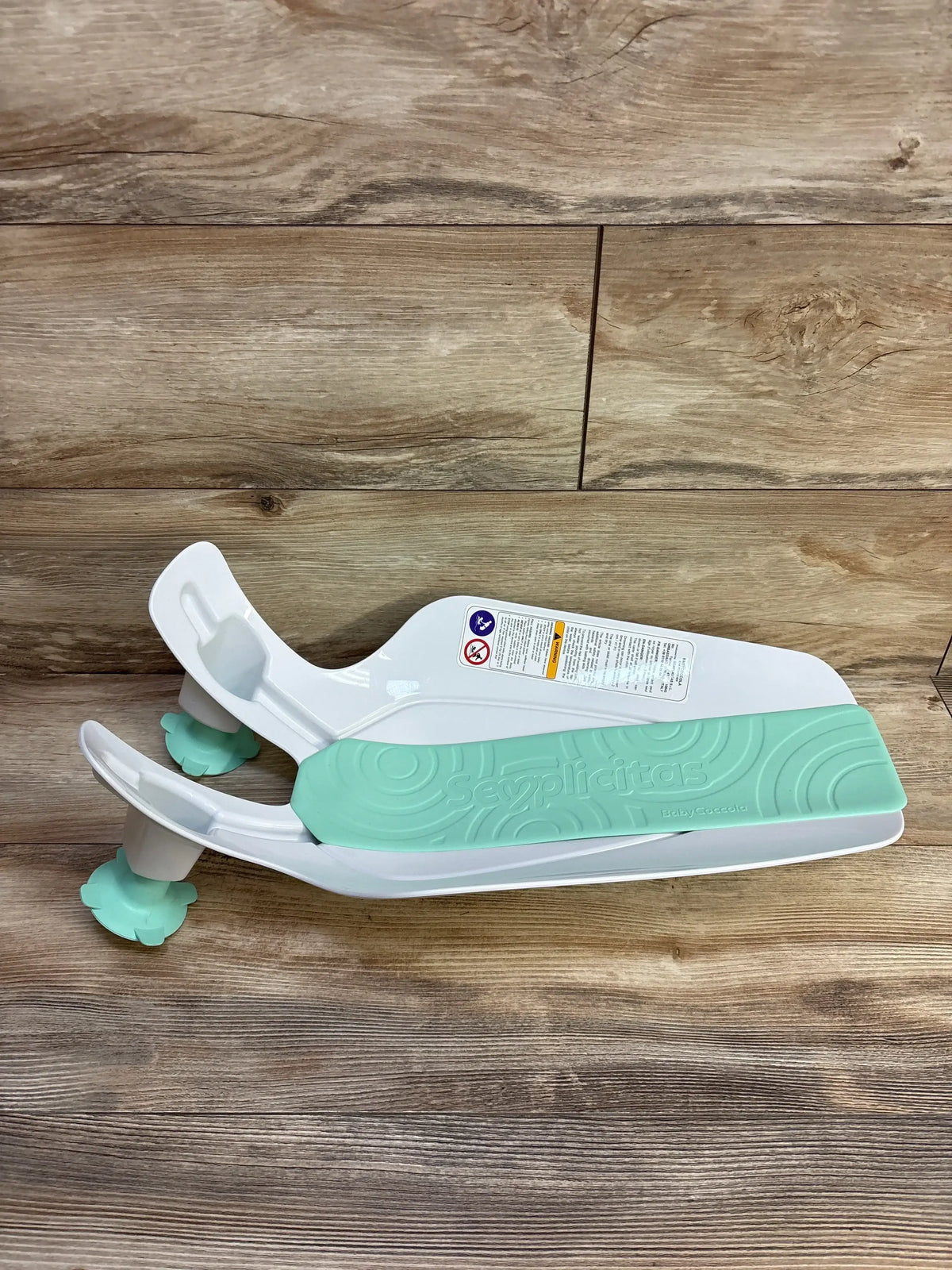 Side view of Semplicitas baby sink bath showcasing mint-green non-slip pad and suction-cup feet on wood plank background