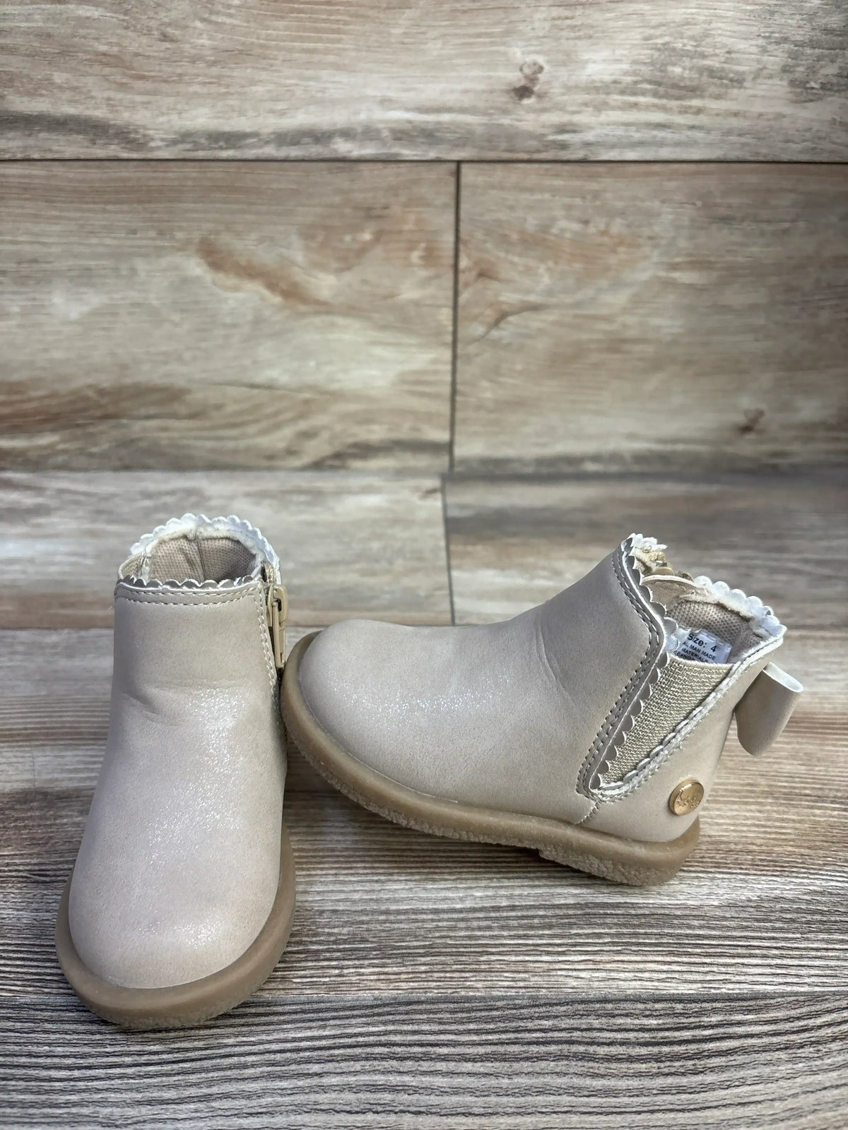 Front and side view of child beige Nicole Miller ankle boots showing scalloped trim and elastic side panel on wood backdrop
