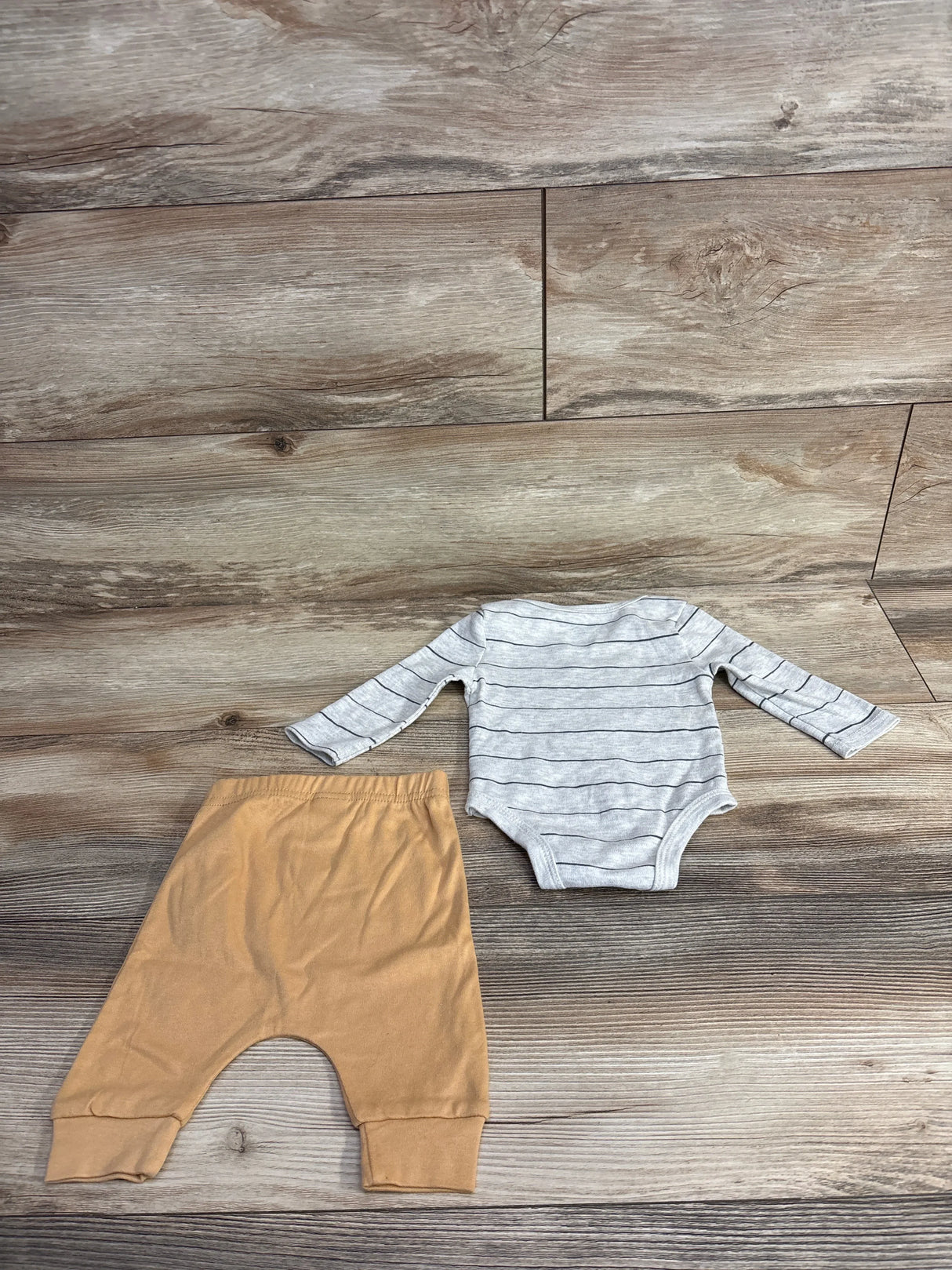 Gray striped long sleeve baby bodysuit with tan baby pants on wood background