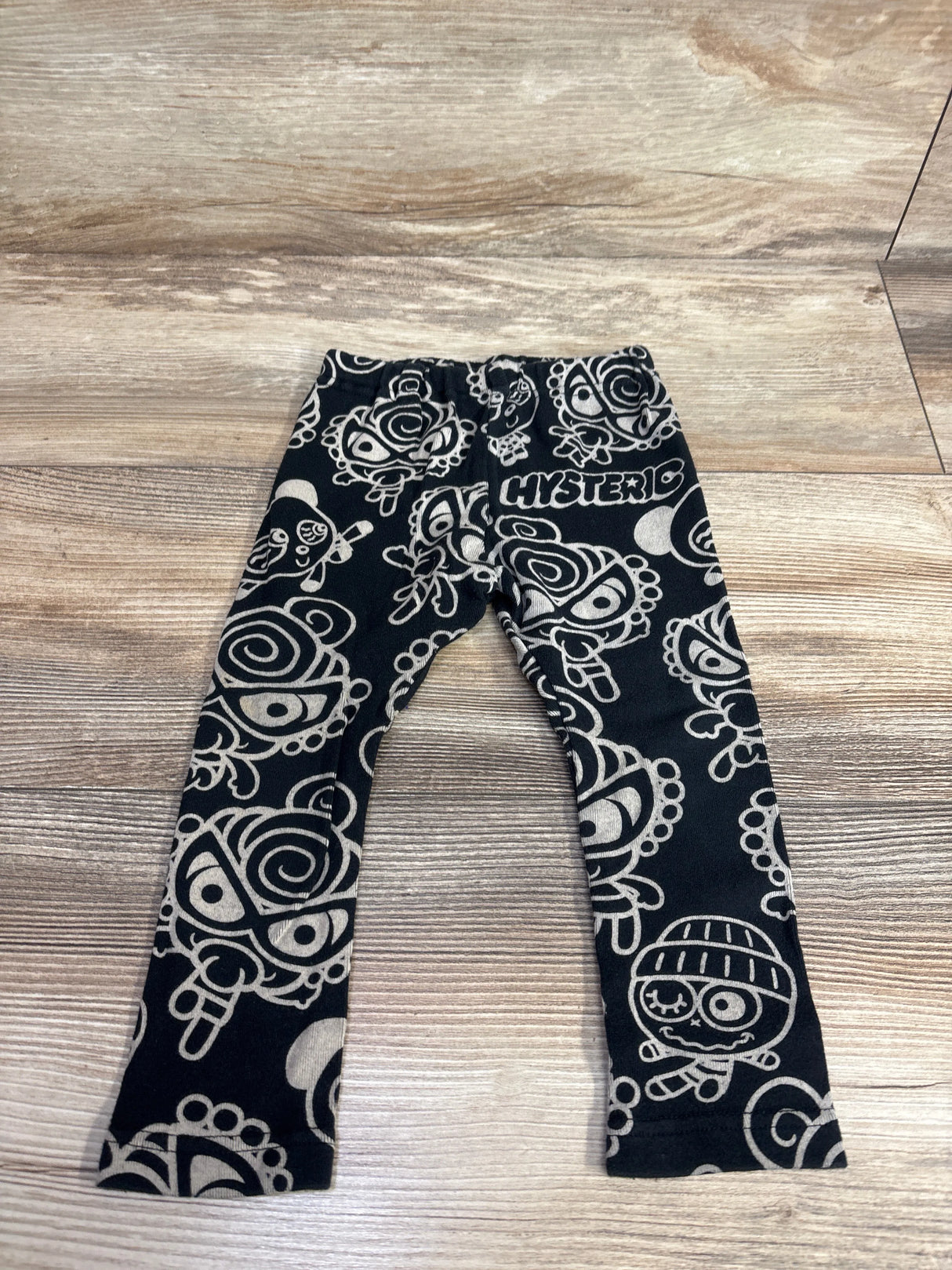Black kids leggings with cartoon faces all-over print on wooden floor
