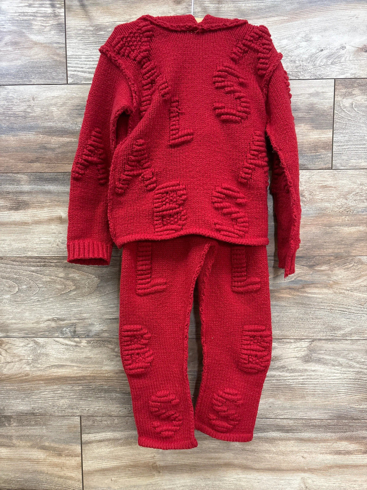 Red knit children's sweater and pants set with textured letter patterns, displayed on wood floor.