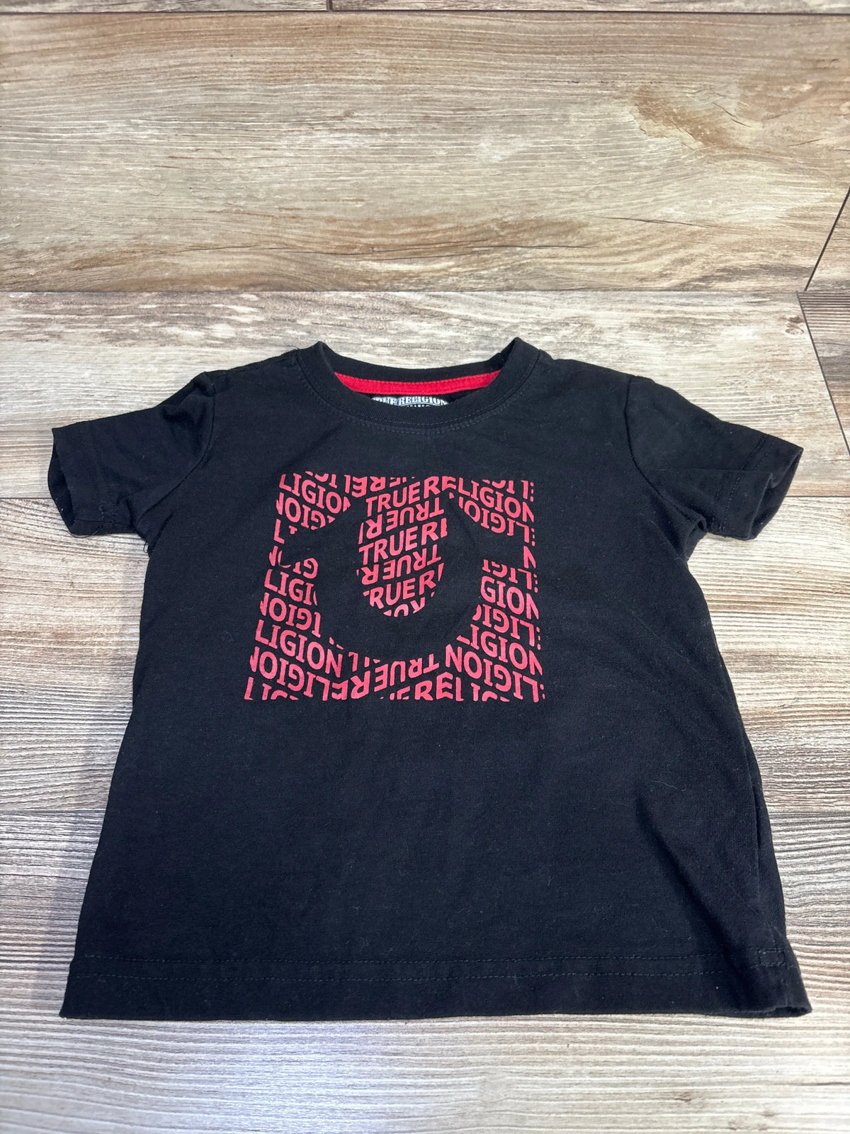 Front view of a black True Religion toddler shirt in size 4T showcasing a pink True Religion horseshoe graphic on a wood surface