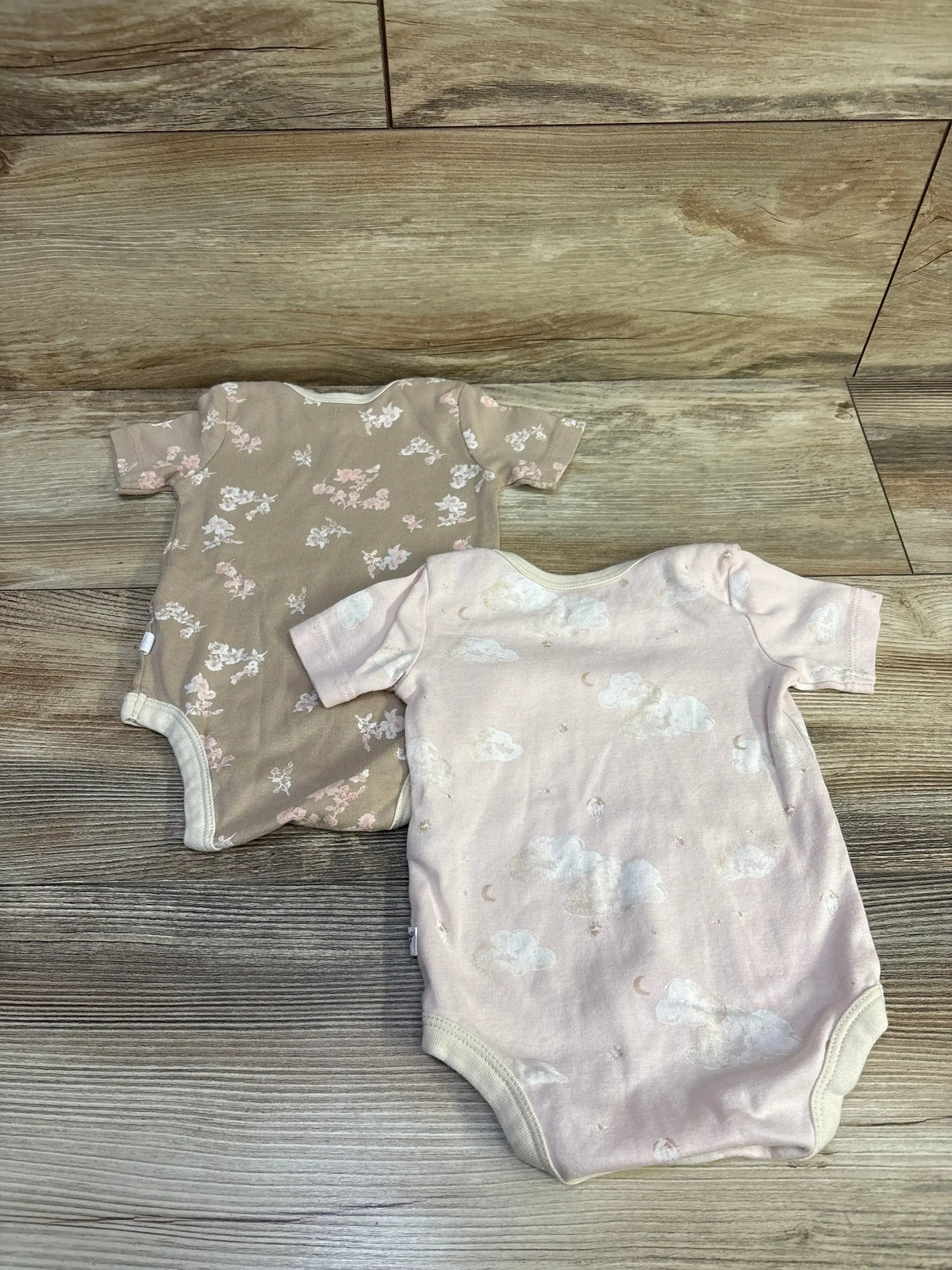 Top view of Burts Bees Baby 2-pack organic cotton bodysuits in pink, with short sleeves and round necks on wood-look floor