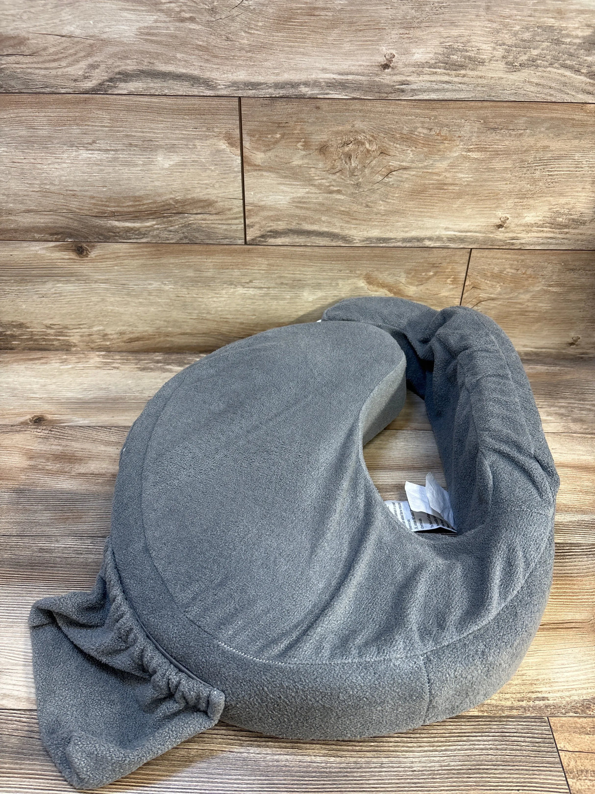 Gray crescent-shaped nursing pillow with soft cover on wooden background