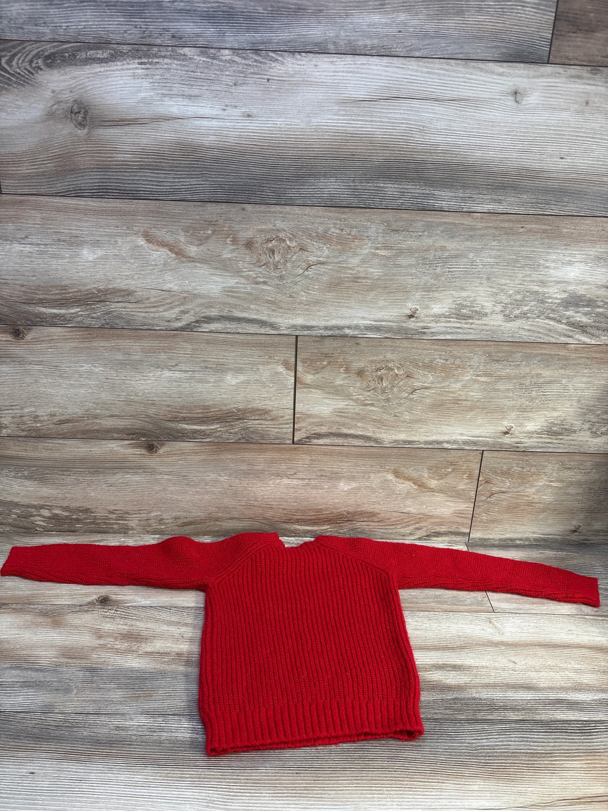 Front flat lay of red shoulder bow sweater showing ribbed knit texture and long sleeves on light wood plank background