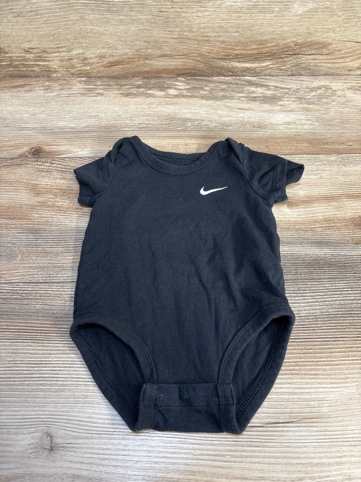 Black Nike baby onesie with white swoosh logo on wooden surface