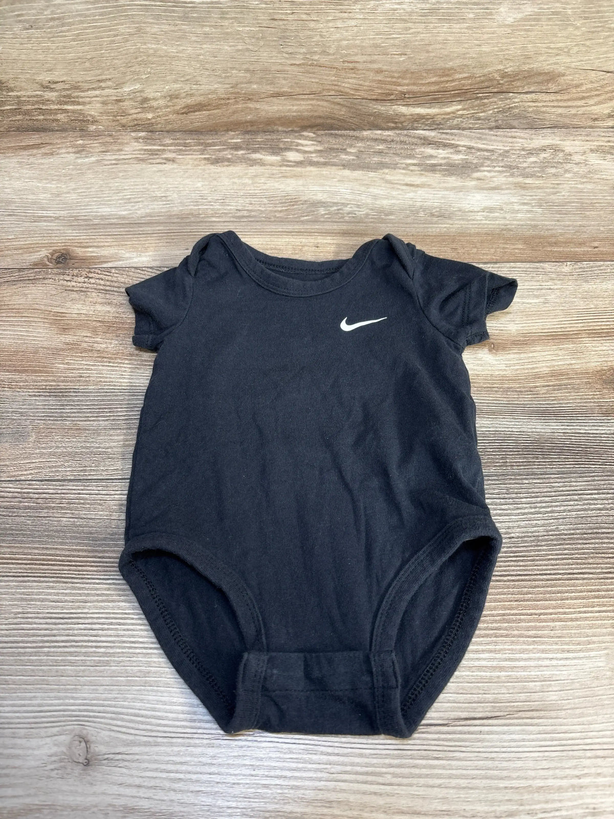 Black Nike baby onesie with white swoosh logo on wooden surface